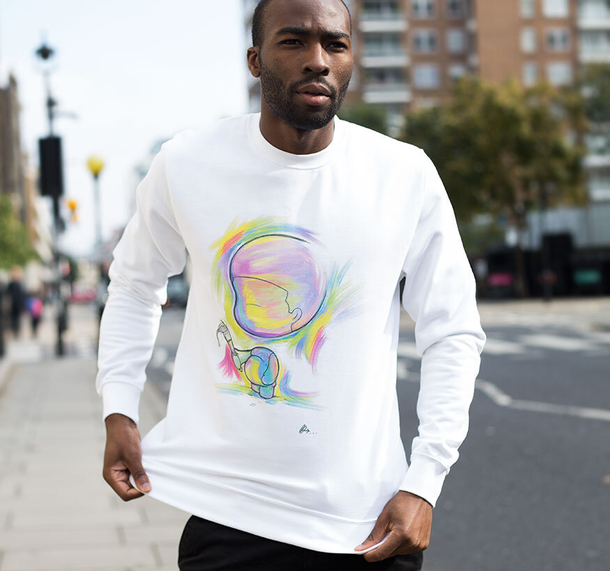 Man wearing a white sweatshirt with colorful abstract rainbow artwork, standing on city sidewalk with buildings and trees in background.