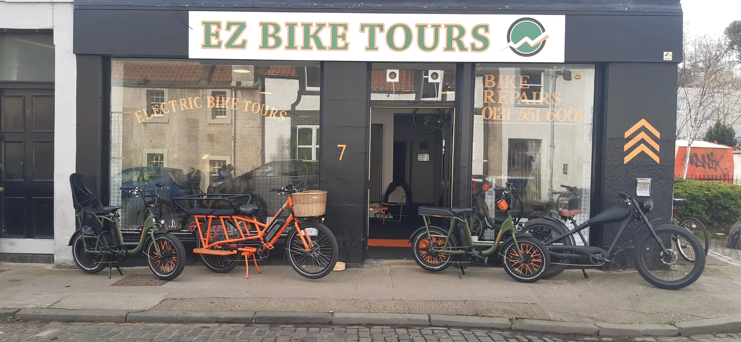 storefront with a sign that reads 'EZ BIKE TOURS' and display of electric bikes parked outside. The store offers electric bike tours and bike repairs, with contact number 0181 551 6001.