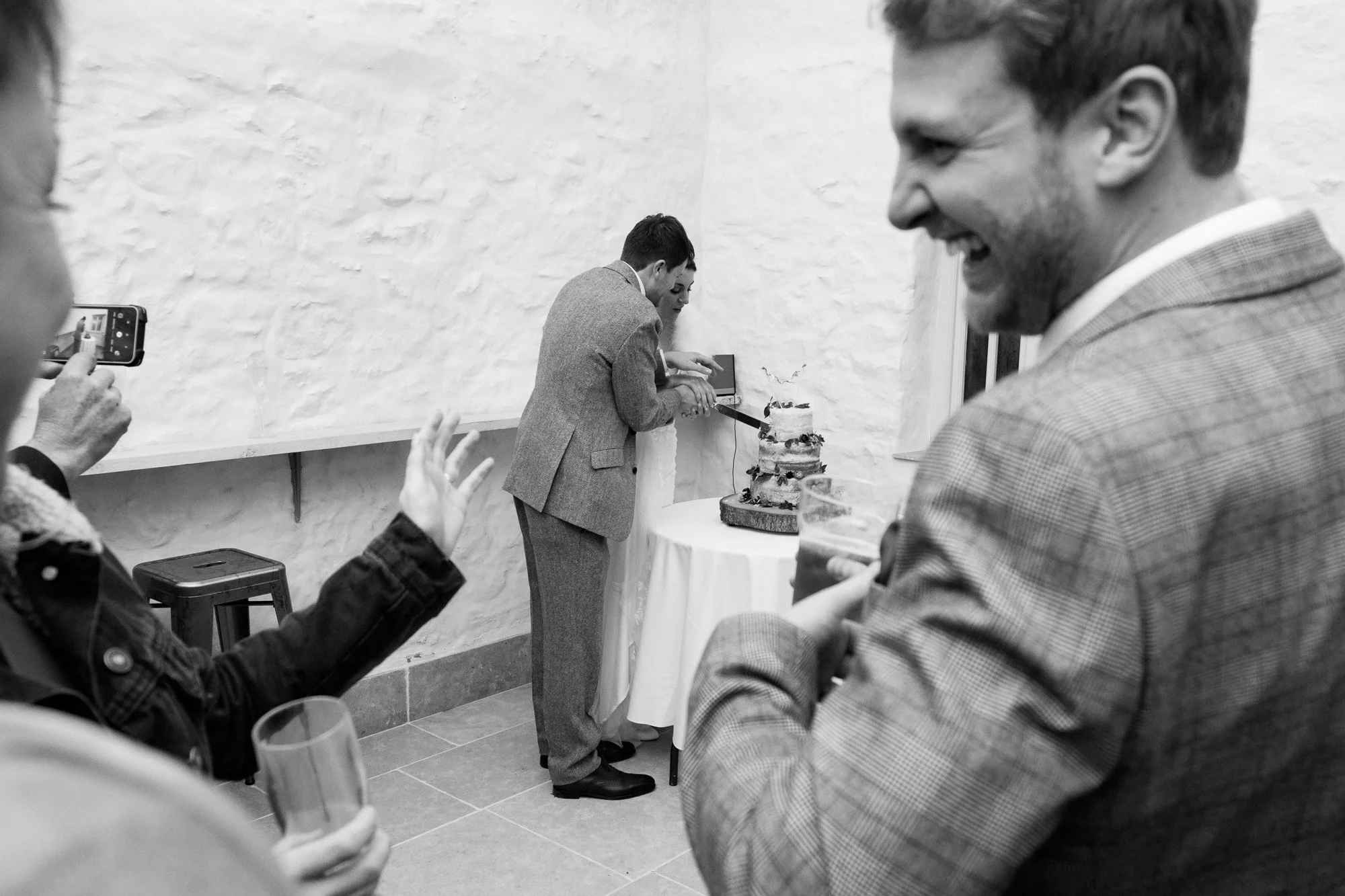 Bride and Groom cut their wedding cake whilst guests watch  at The Great Barn, Exeter, Devon.