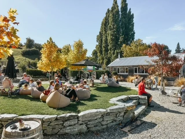 People relaxing and enjoy a coffee and wine on Bill's Green at Country Lane Retail Village in Frankton, Queenstown.