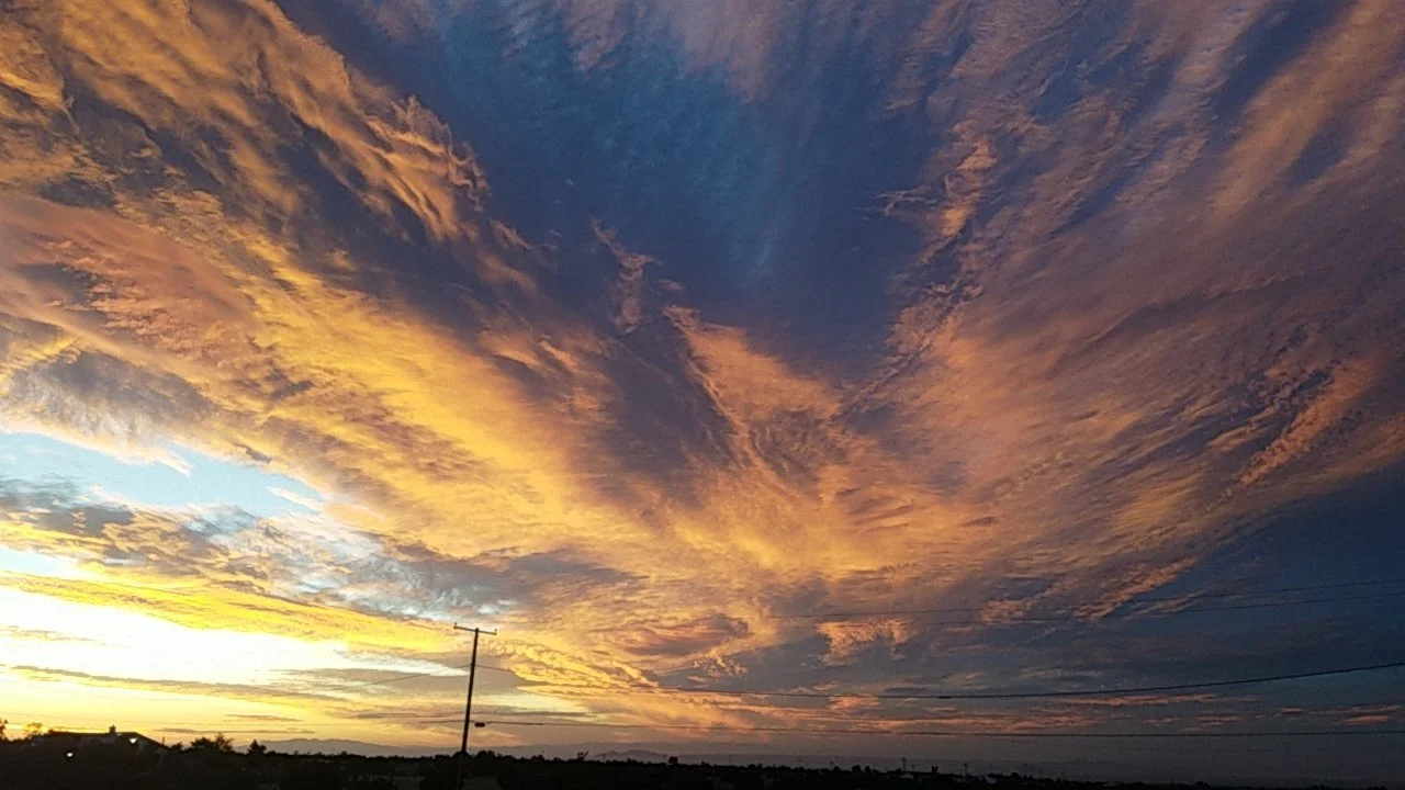 Dramatic sunset sky with orange, pink, and blue clouds over a rural landscape, with a silhouette of power lines.