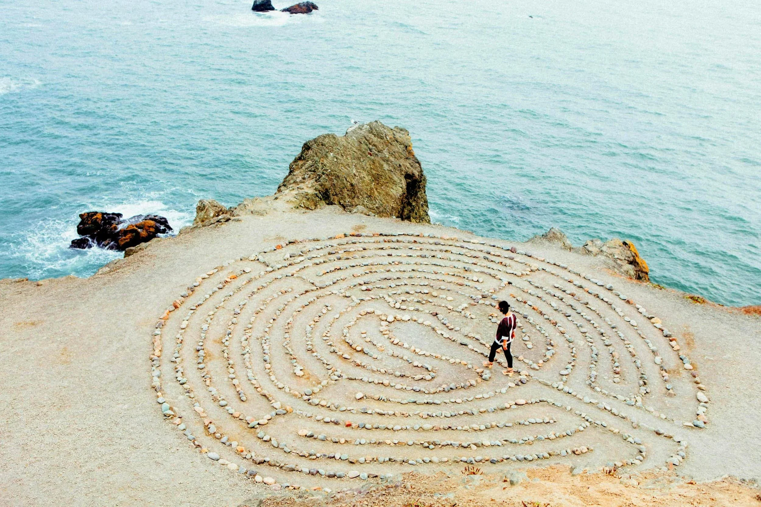 Woman walking along a sprial maze made of stones on a beach cliff