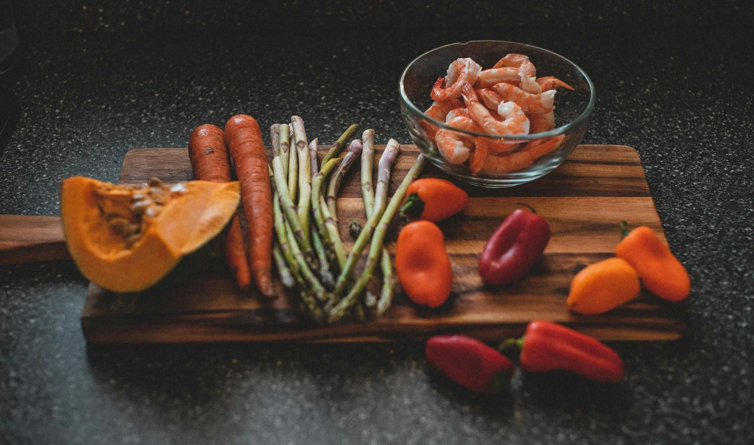 Cutting board with meal prep of shrimp, peppers, asparagus, carrot and squash