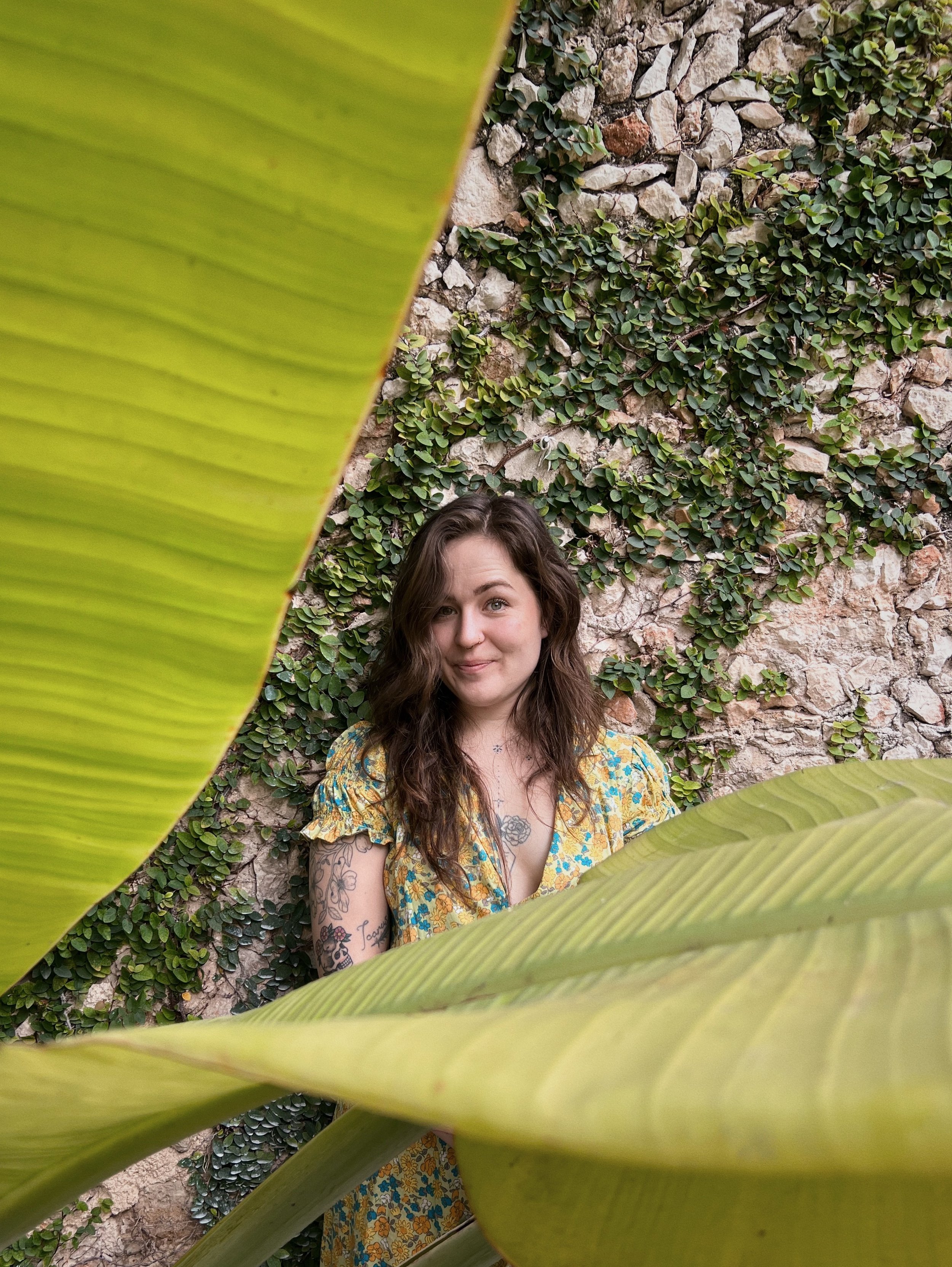 Portrait of Angelene, owner of Villanelle Floral, in a green dress that matches tropical surroundings.