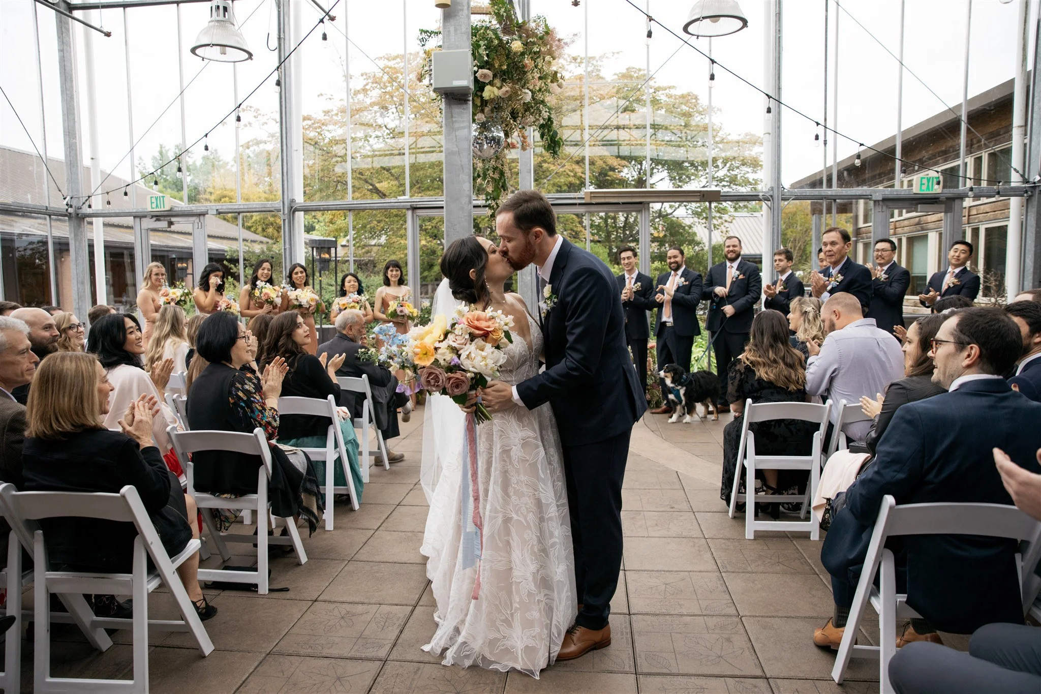 A lush, suspended floral installation and matching bridal bouquet of garden roses, poppies, blooming branches, and delphinium in Seattle green house.