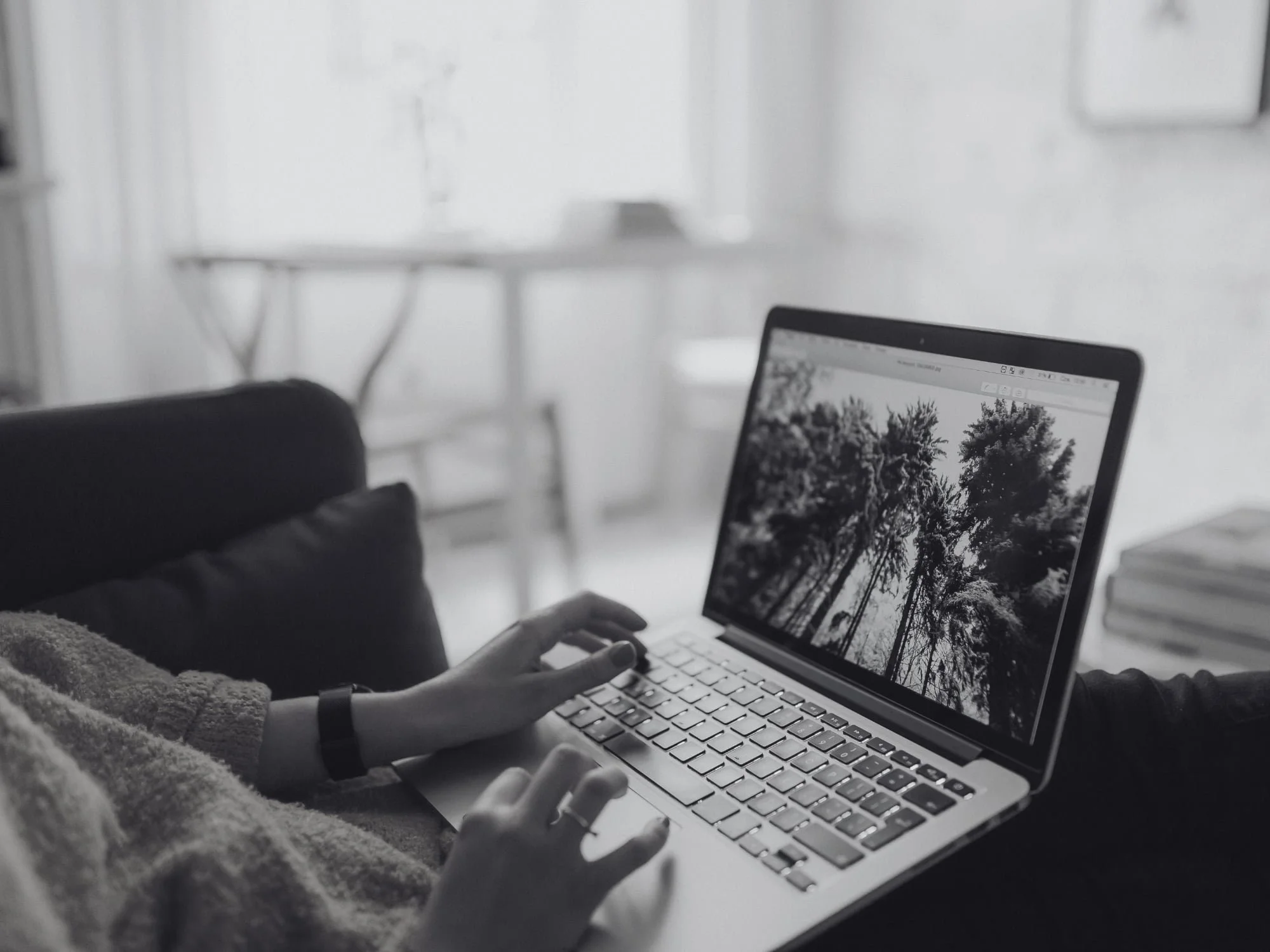 Squarespace web designer using a laptop building a squarespace website on a couch, viewing a black-and-white photo of trees on the screen.