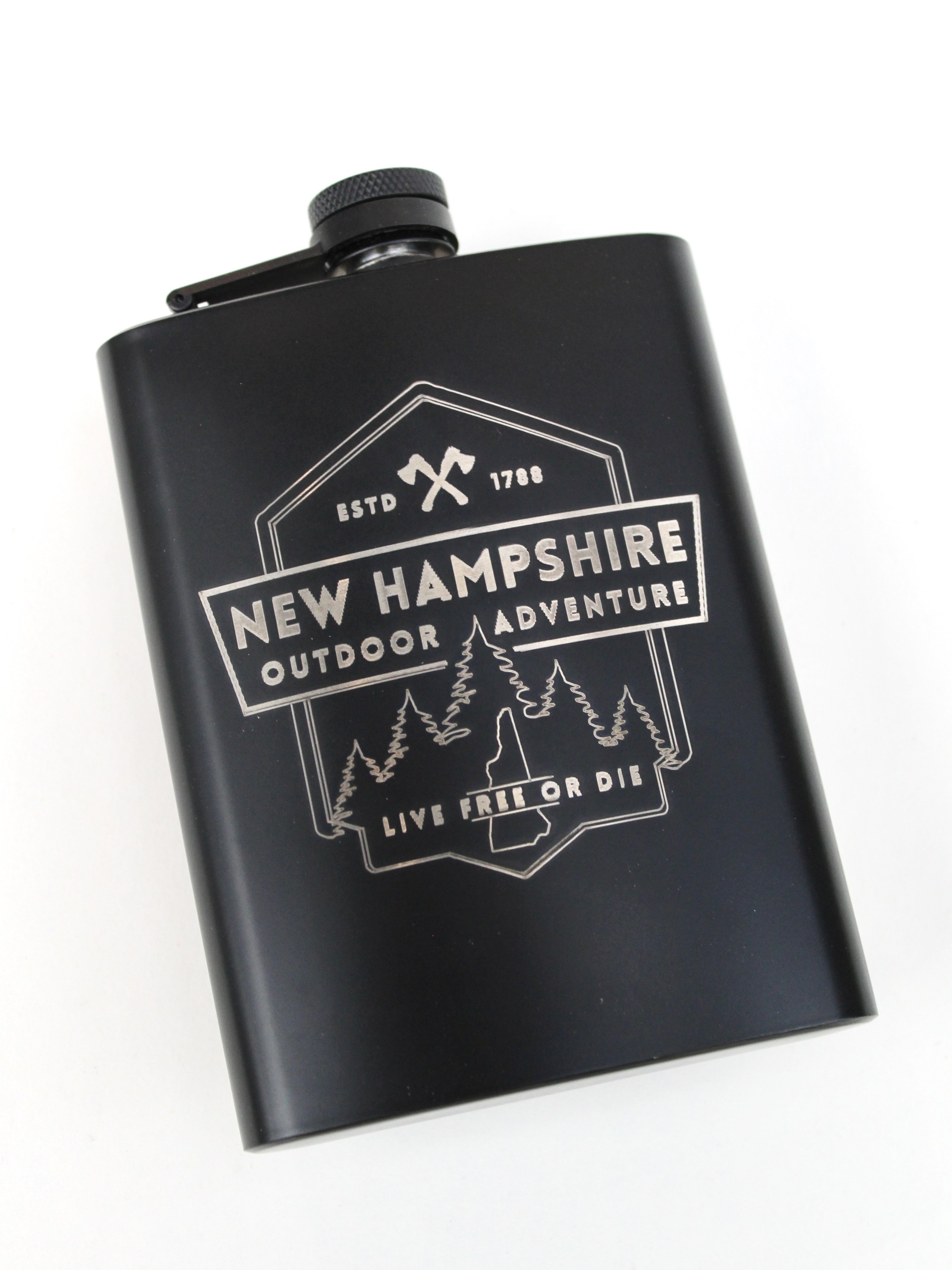 Black beverage flask with New Hampshire, Live Free or Die etched on the front with mountains in the background.