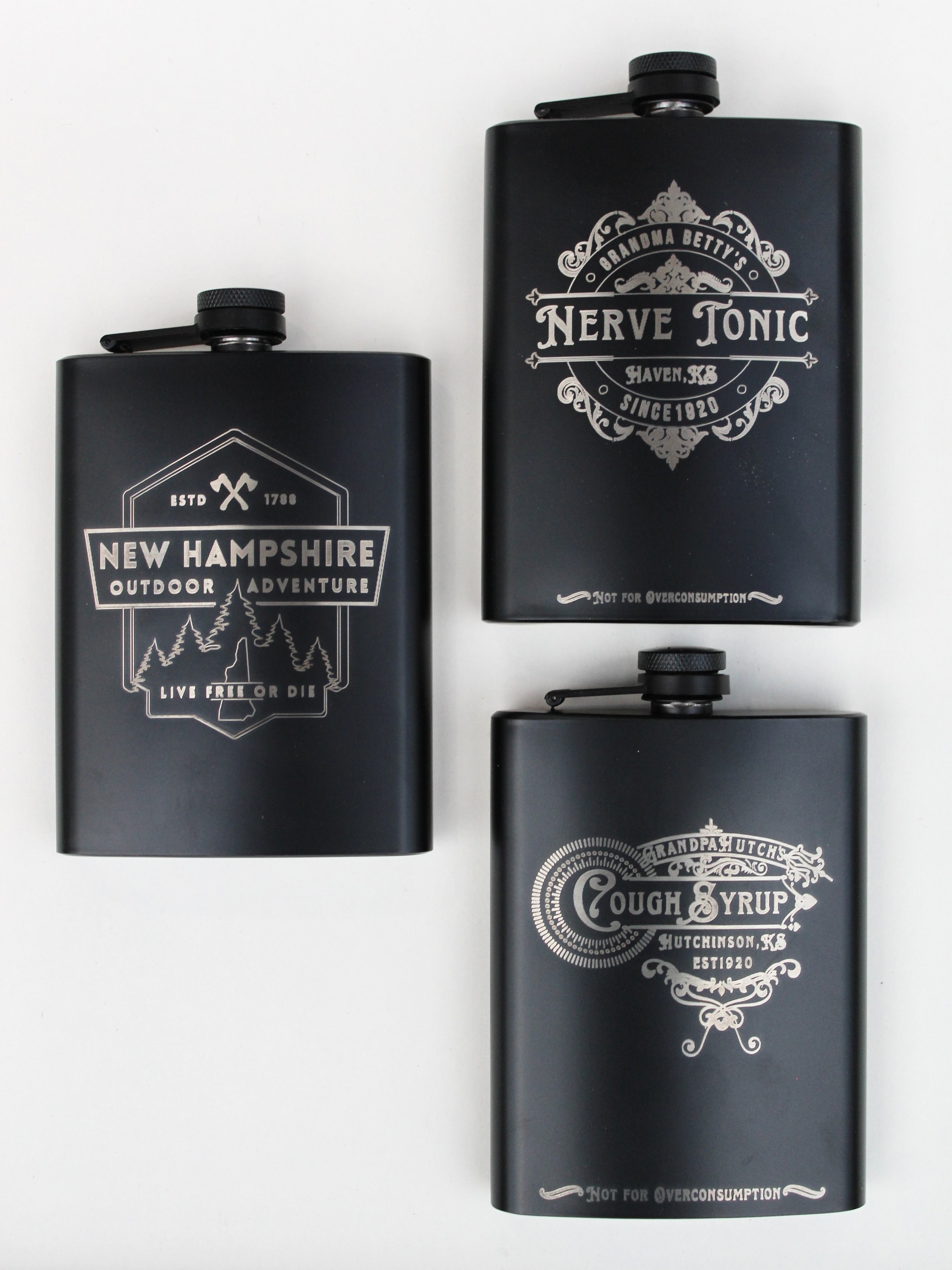 Three beverage flasks laying down. The picture is taken from the top looking down. The three flasks all have silver monogrammed wording and designs.
