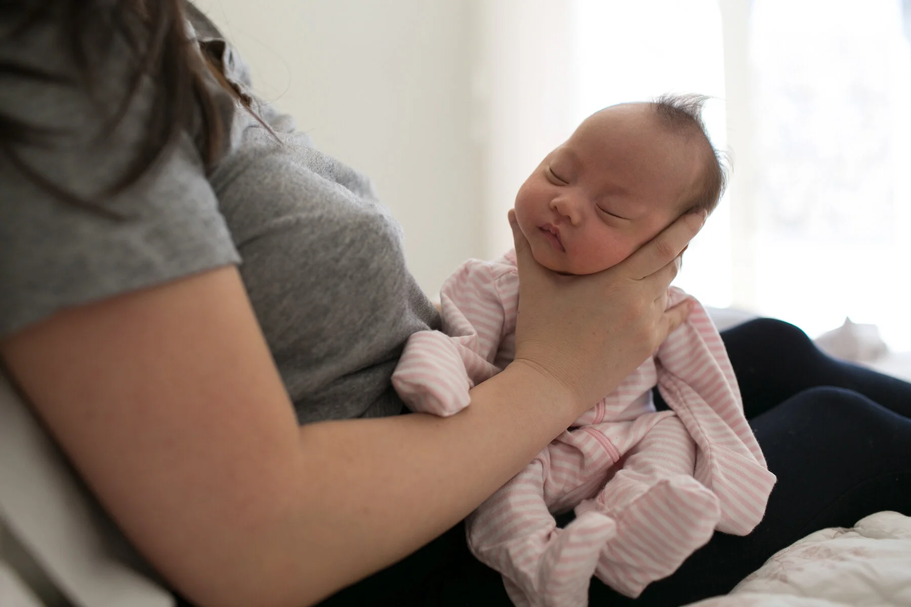 Person holding a sleeping baby wearing a pink and white striped outfit.