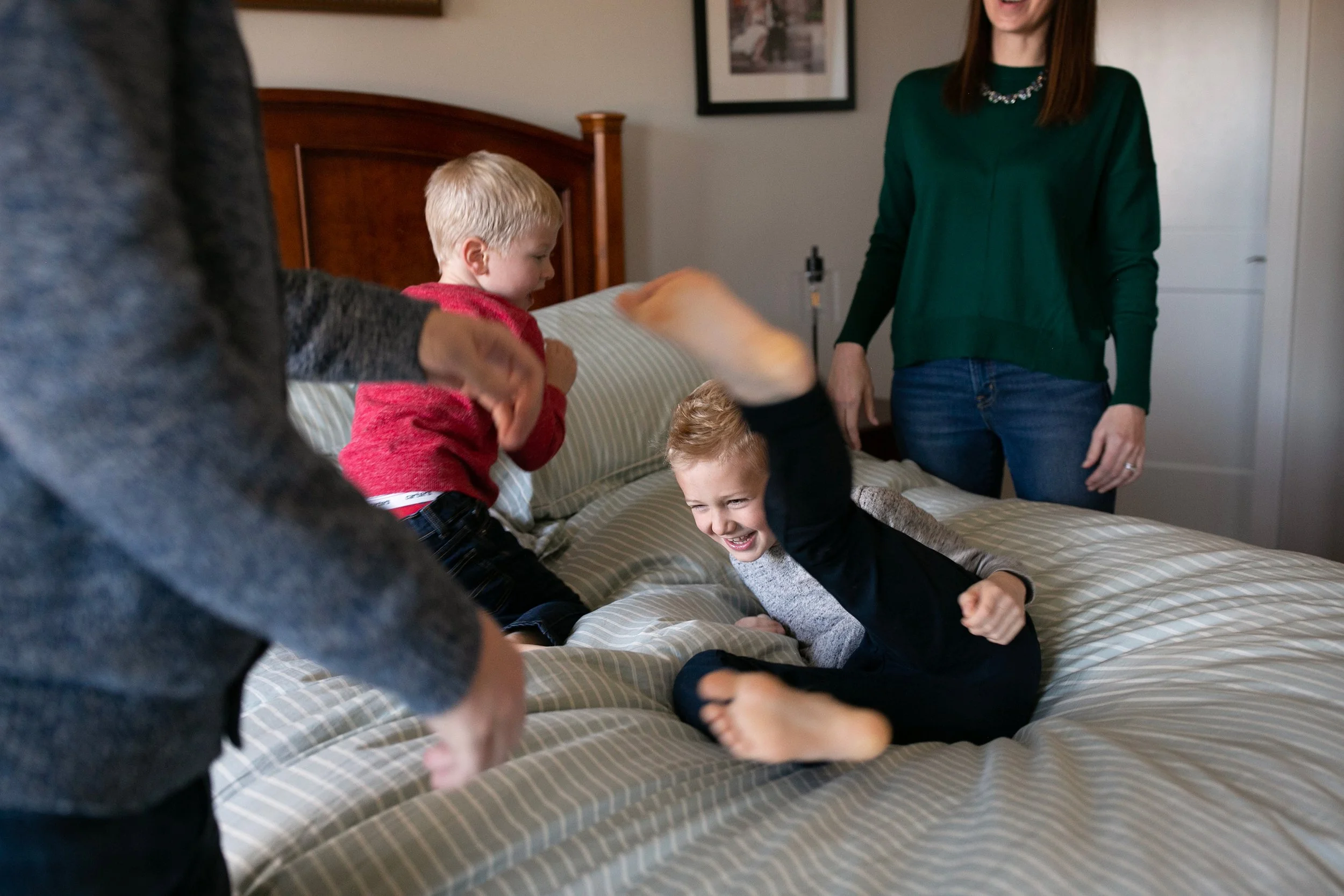 Family playing and laughing on a bed, featuring two children and two adults.