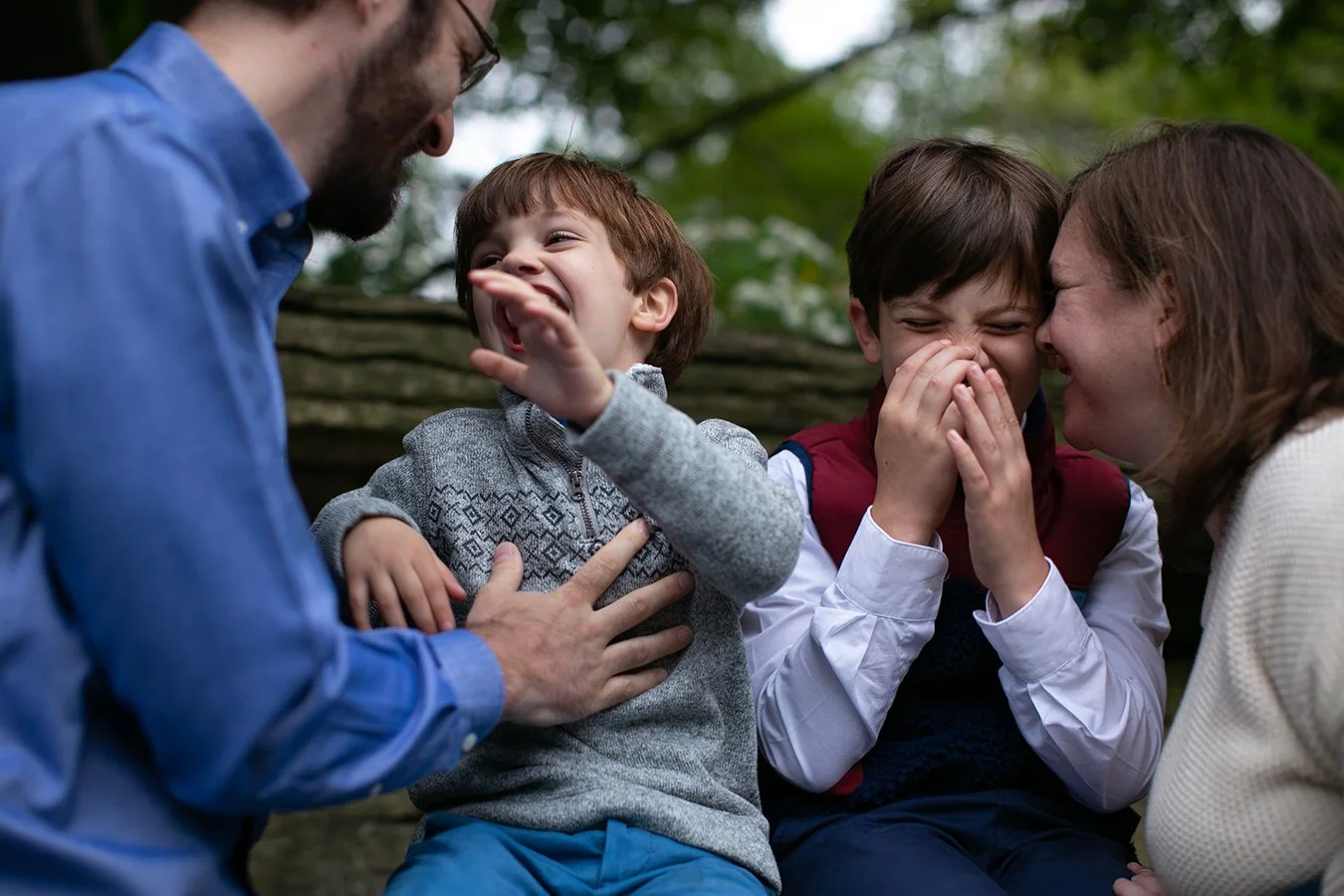 Family enjoying a playful moment outdoors, two parents and two children laughing and smiling.