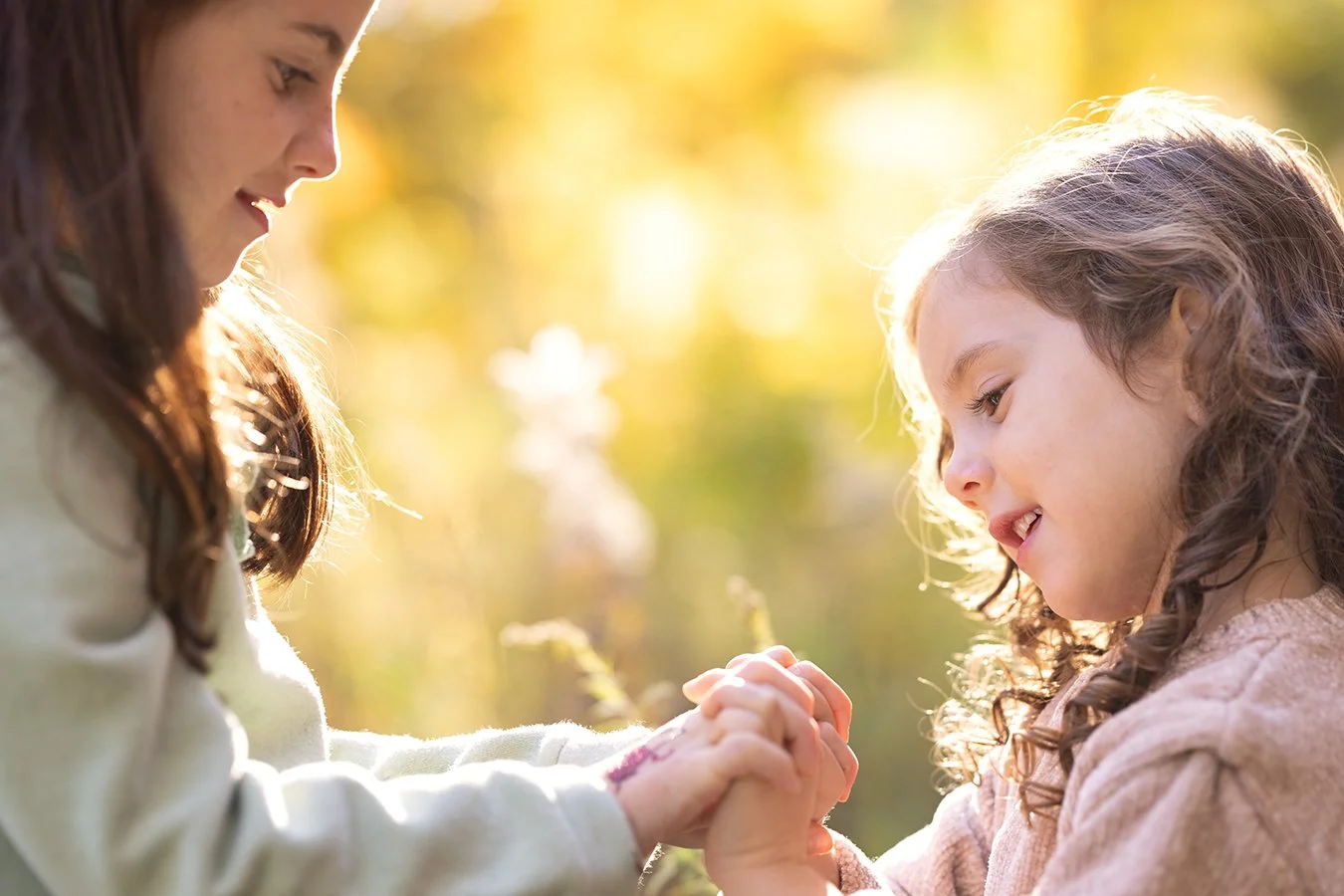 Two young girls holding hands in a sunlit outdoor setting.