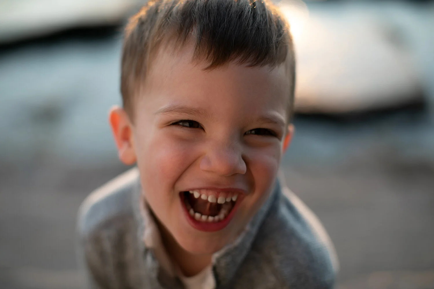 A young child laughing with an open mouth, wearing a gray sweater, outdoors.
