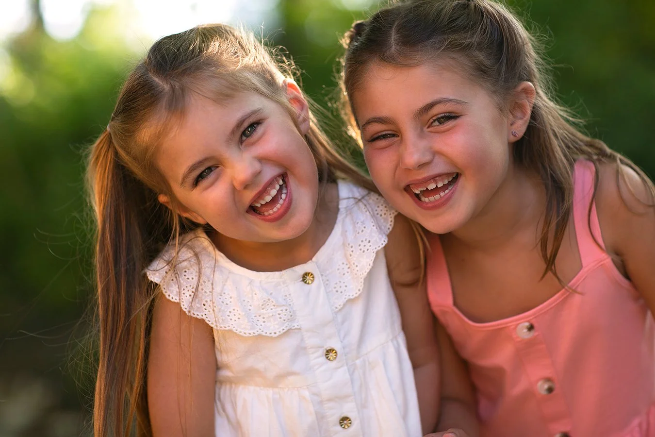 Two young girls smiling and laughing outdoors.