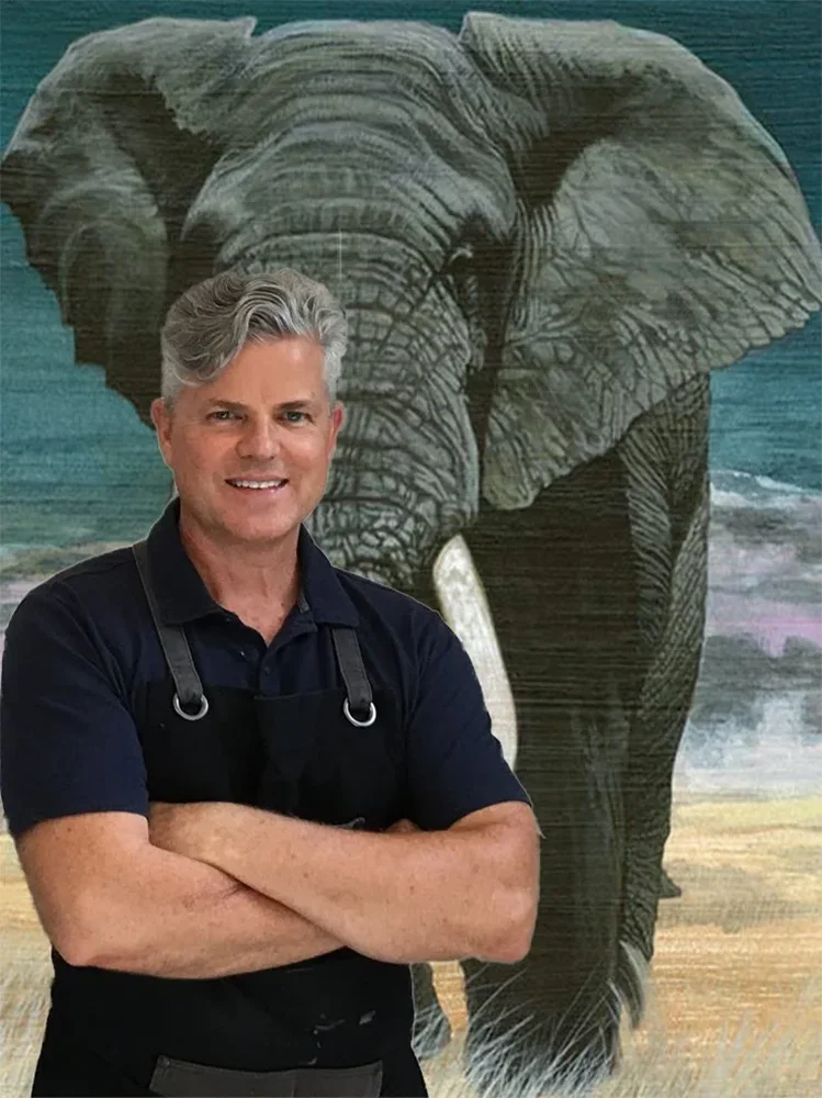 Clint Eagar, wildlife fine art painter, standing in his studio in front of a large-scale African elephant acrylic painting.