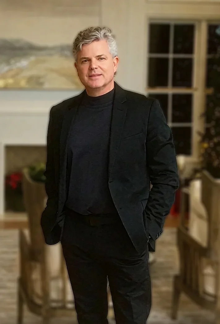 Clint Eagar, fine artist and gallery owner on 30A, formal portrait in an elegant interior with artwork visible in the background.