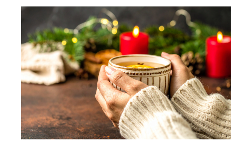 hands holding tea mug with red candles in the background
