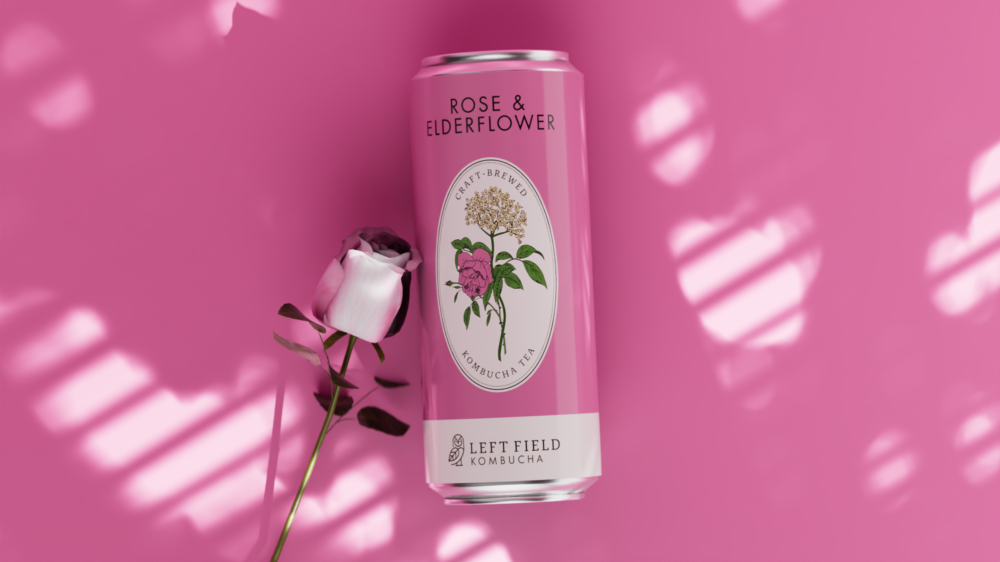 A pink can of Left Field Kombucha tea labeled 'Rose & Elderflower,' with an illustration of a flowering plant, positioned on a pink background with shadow patterns and a pink rose.