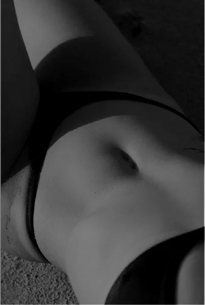 Close-up of a person's midsection, wearing black underwear, lying down on a textured surface.