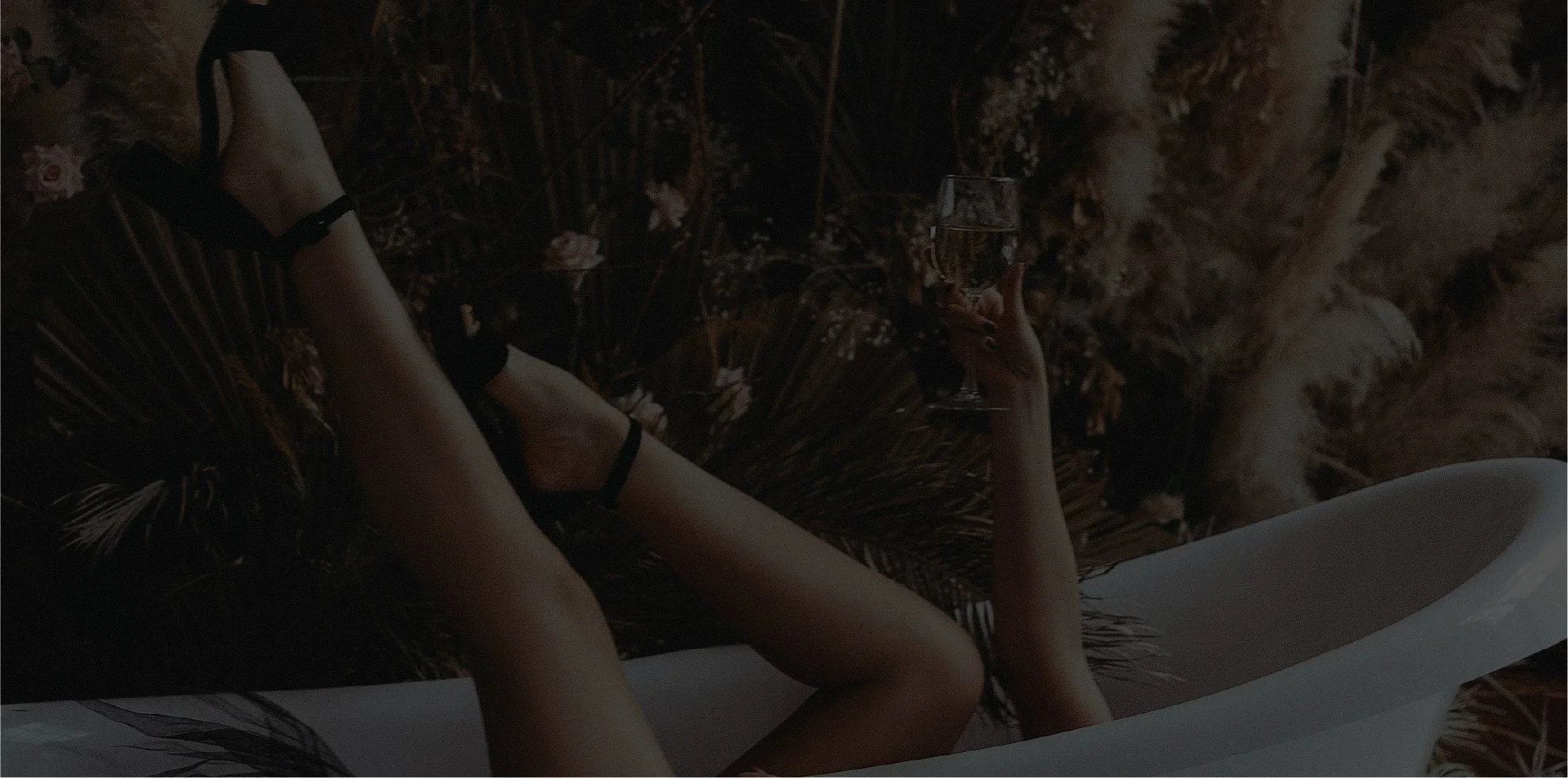 Woman in a bathtub with legs sticking out, wearing heels and holding a glass of wine.