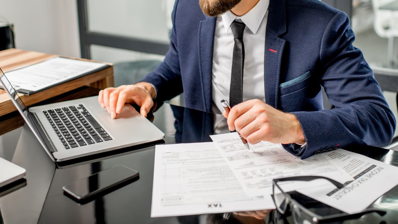 Businessman in a suit sitting at a desk working with documents and a laptop