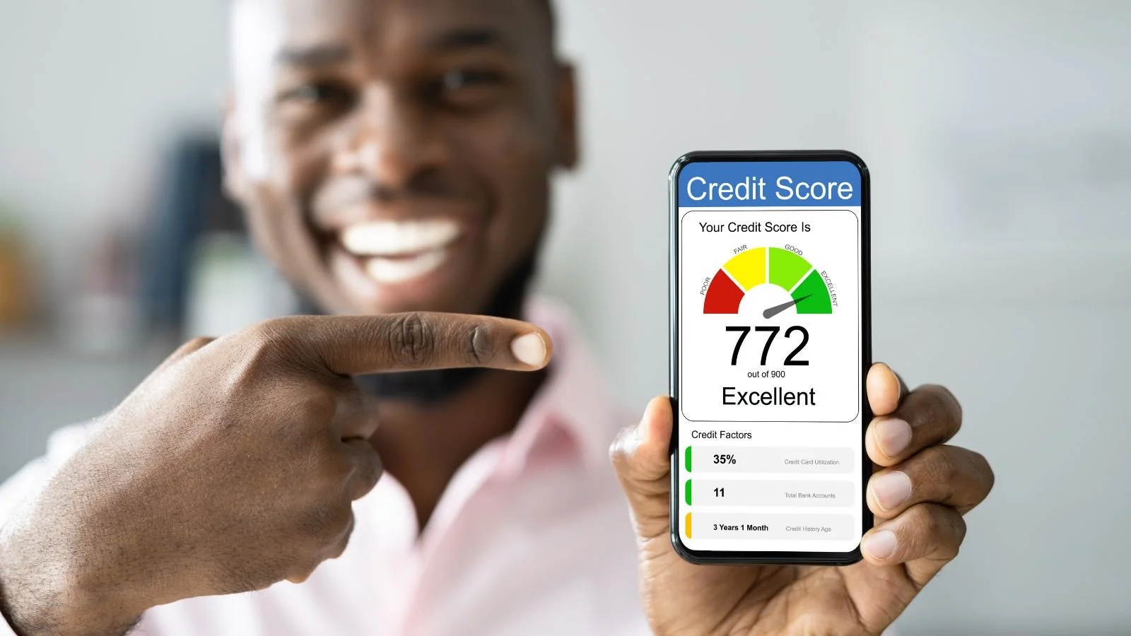 Man smiling and pointing at a smartphone displaying a credit score of 772 out of 900, rated as excellent, with credit factors including utilization, bank accounts, and age.