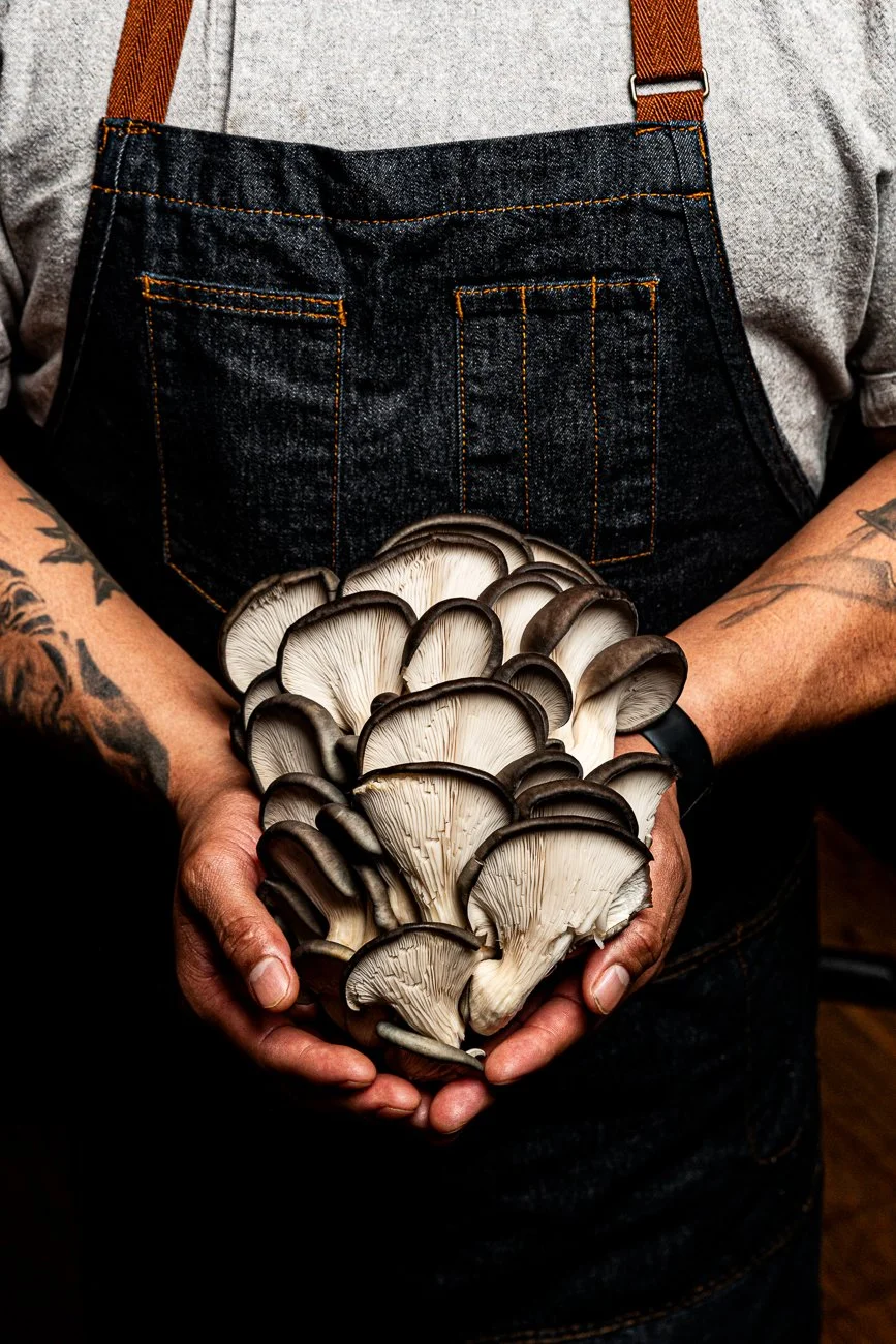 A person wearing an apron and holding a bunch of fresh mushrooms.