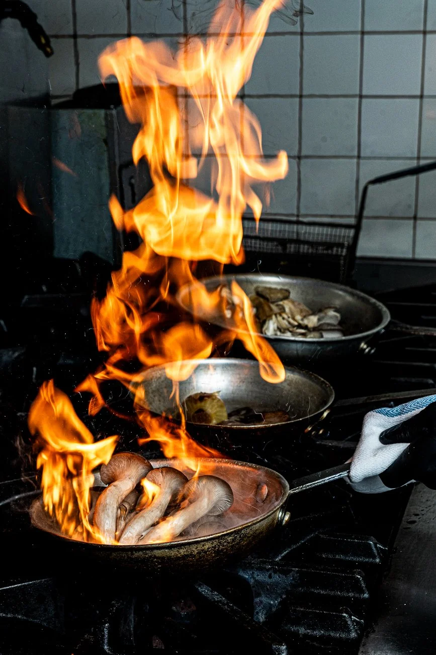 Frying mushrooms in a pan with flames from the burner while cooking in a kitchen.
