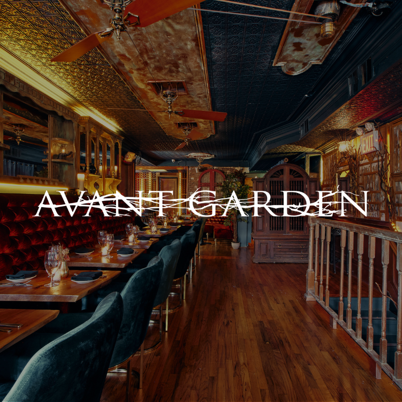 Interior of a restaurant called Avant Garden with dim lighting, wooden floors, plush chairs, tables set with glasses and napkins, ornate ceiling, and decorative elements along the walls.