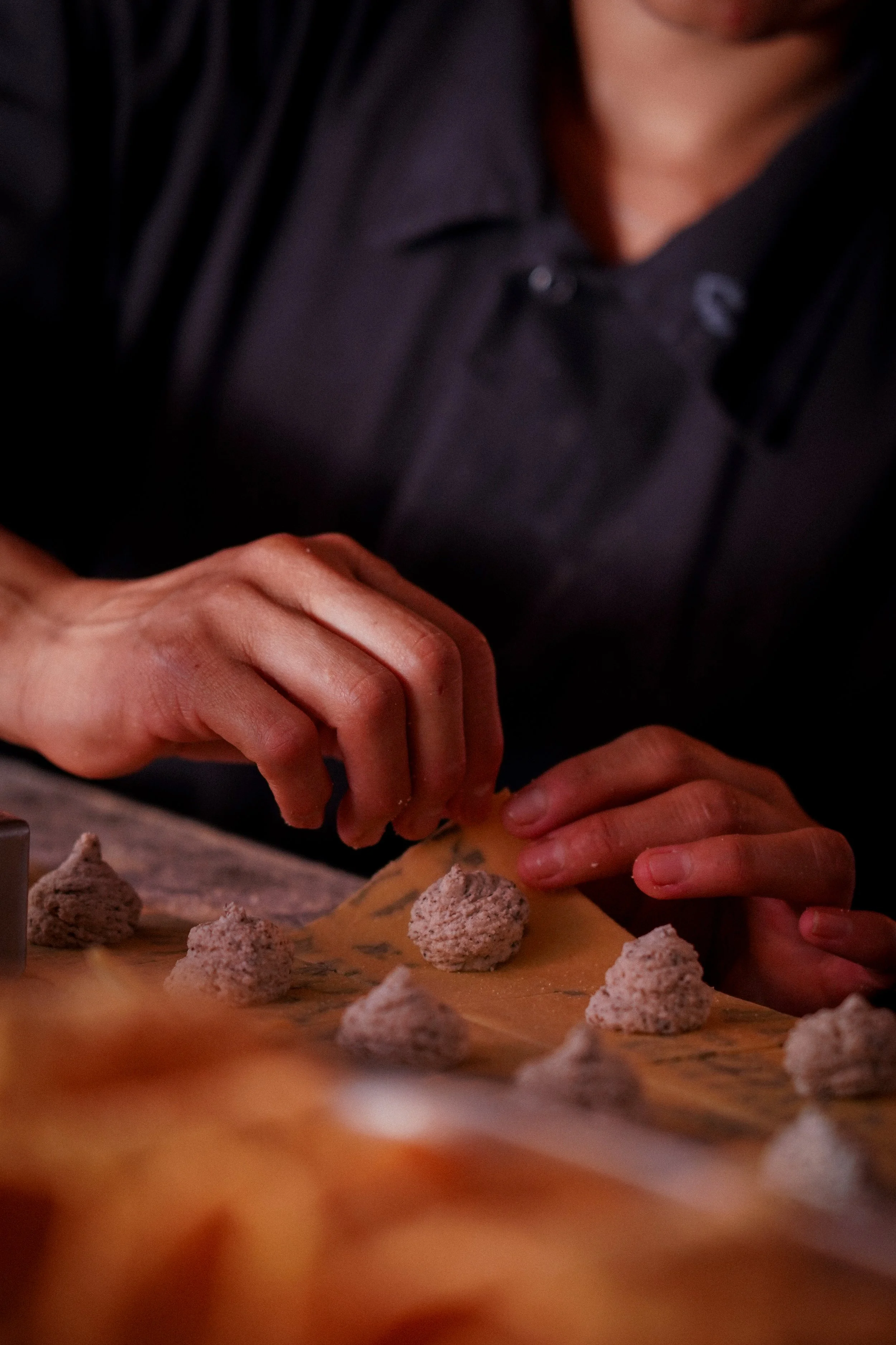 A person working with dough, shaping small pieces into mounds on a wooden surface.