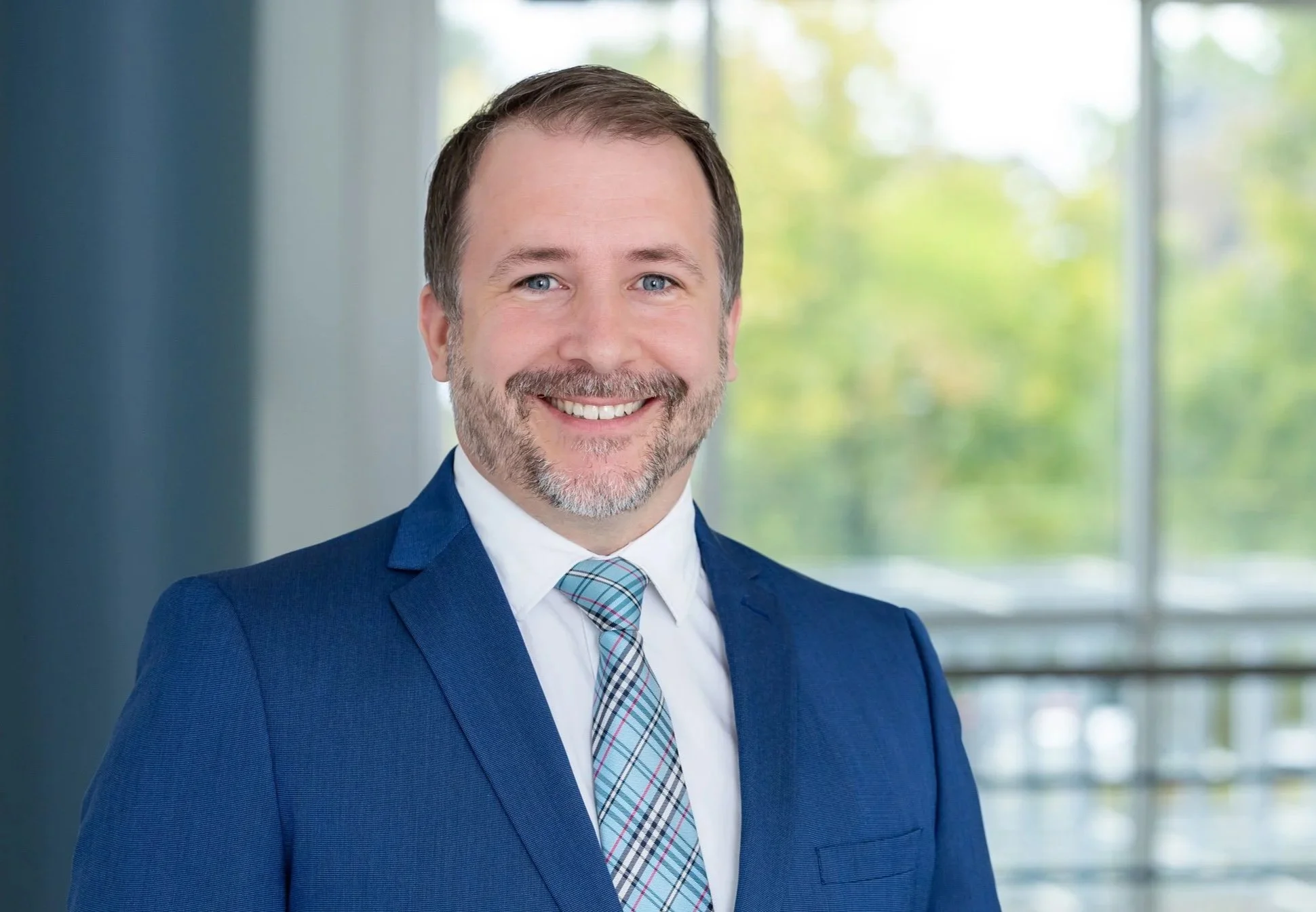 Businessporträt eines Mannes im blauen Anzug vor heller moderner Büroarchitektur.