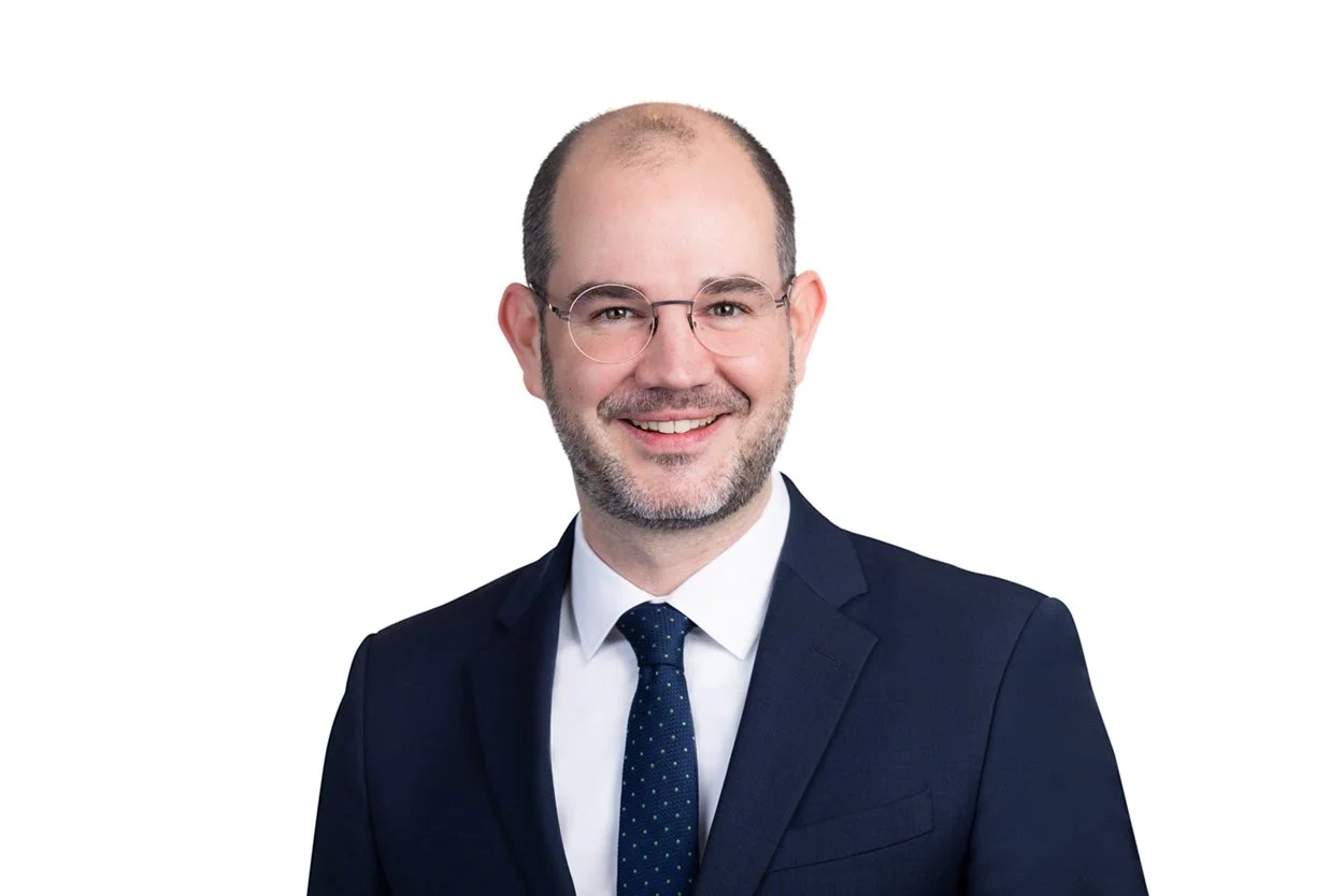 Businessporträt eines Mannes im dunklen Anzug mit Krawatte vor weißem Hintergrund.
