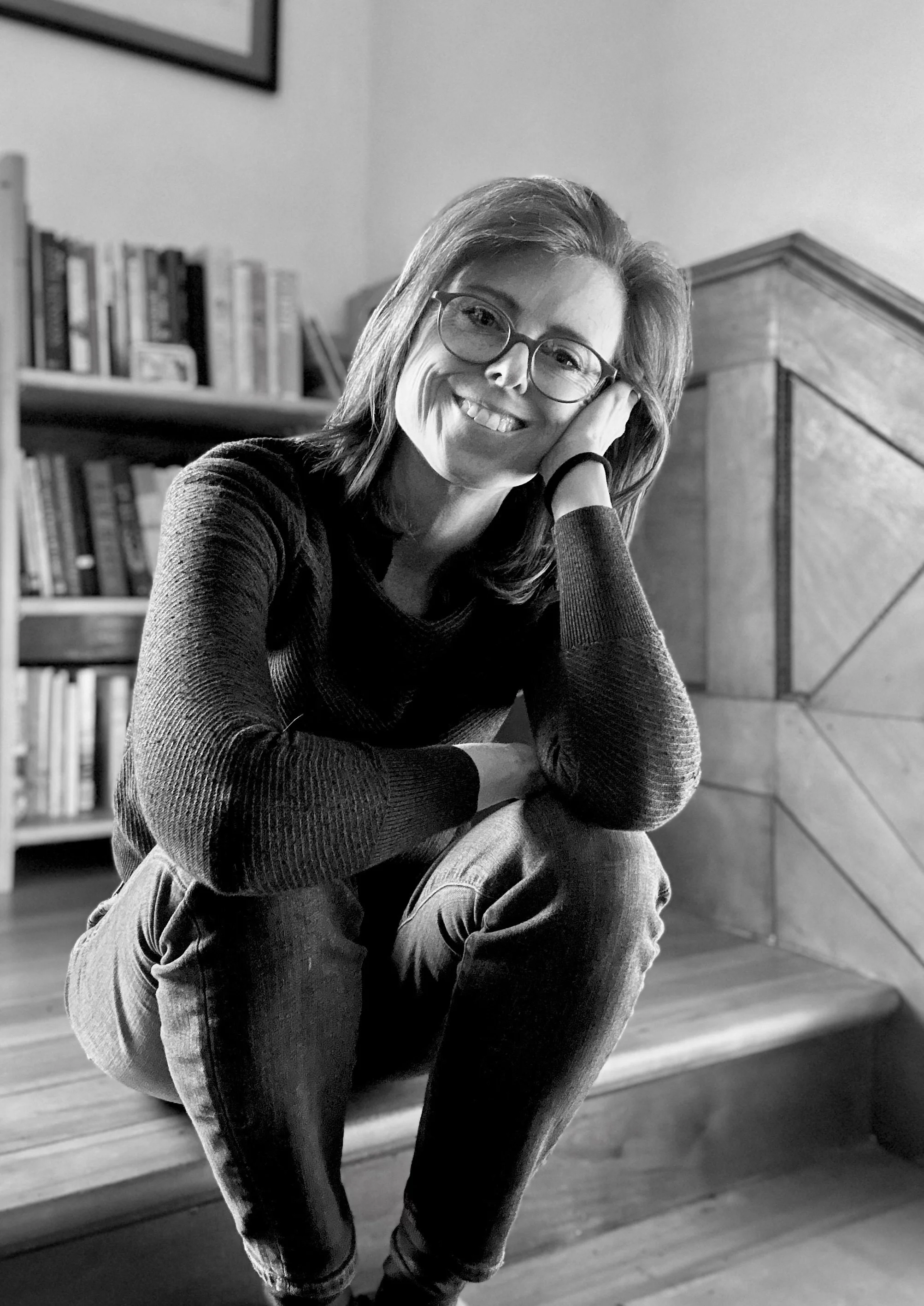 black and white image of a woman sitting on a step with books behind her