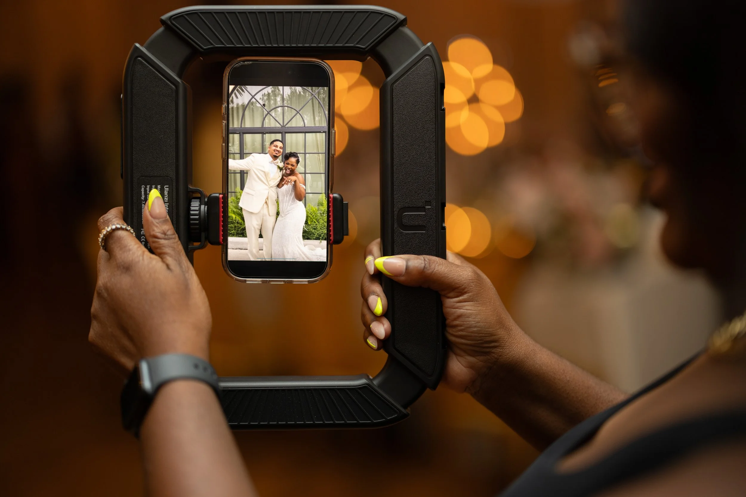 Person taking a photo of a happy couple through a camera viewfinder at their wedding.