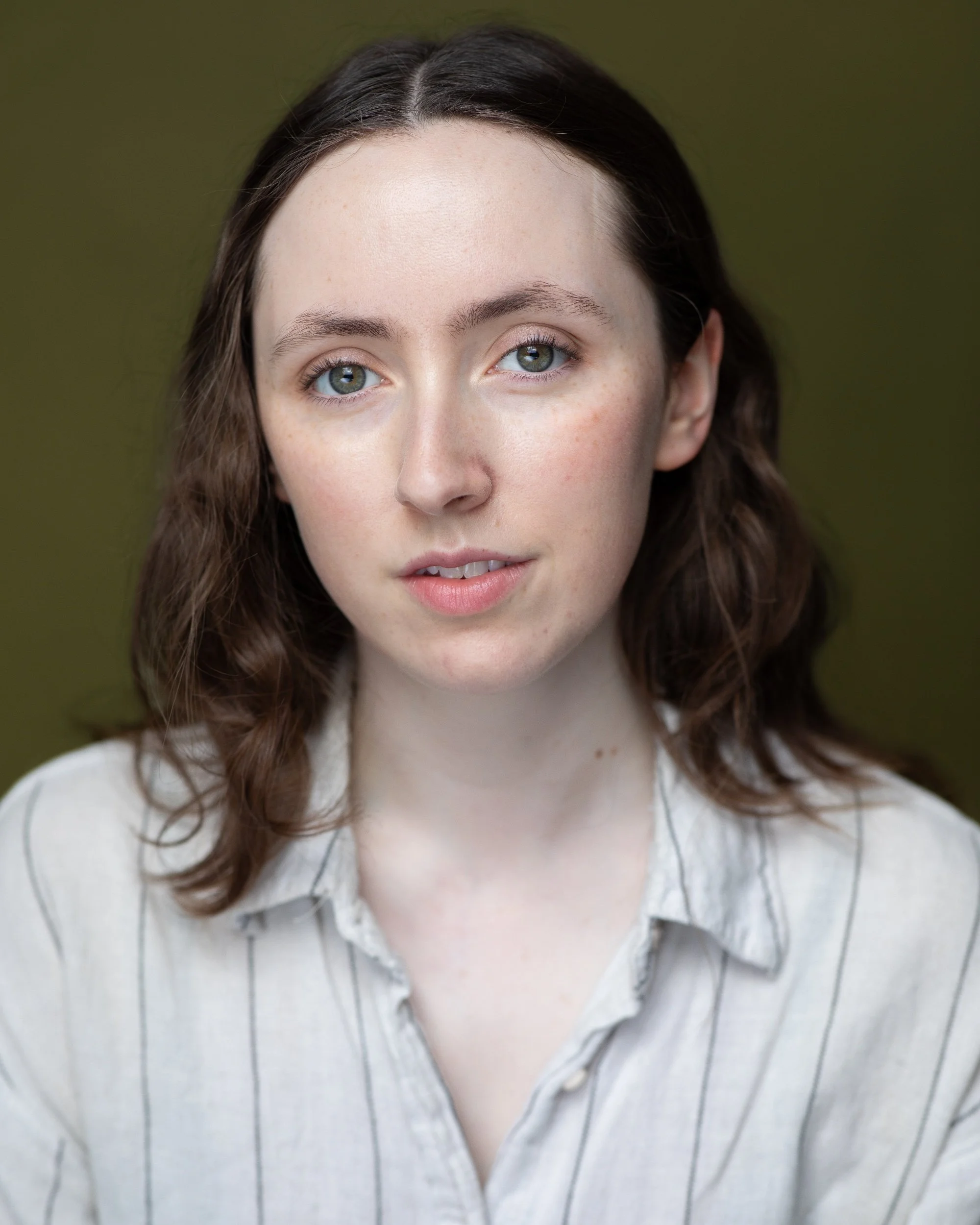 A person with long brown hair wearing a light-colored, striped shirt against a green background.