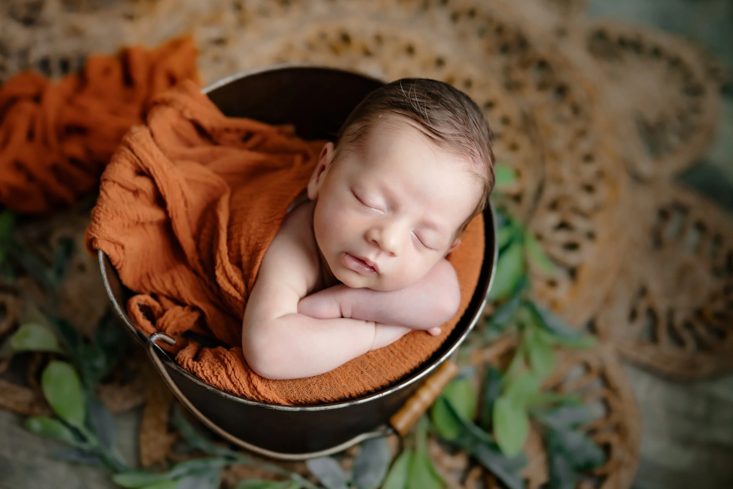 newborn boy resting peacefully on his hands in a bucket during an in home newborn session