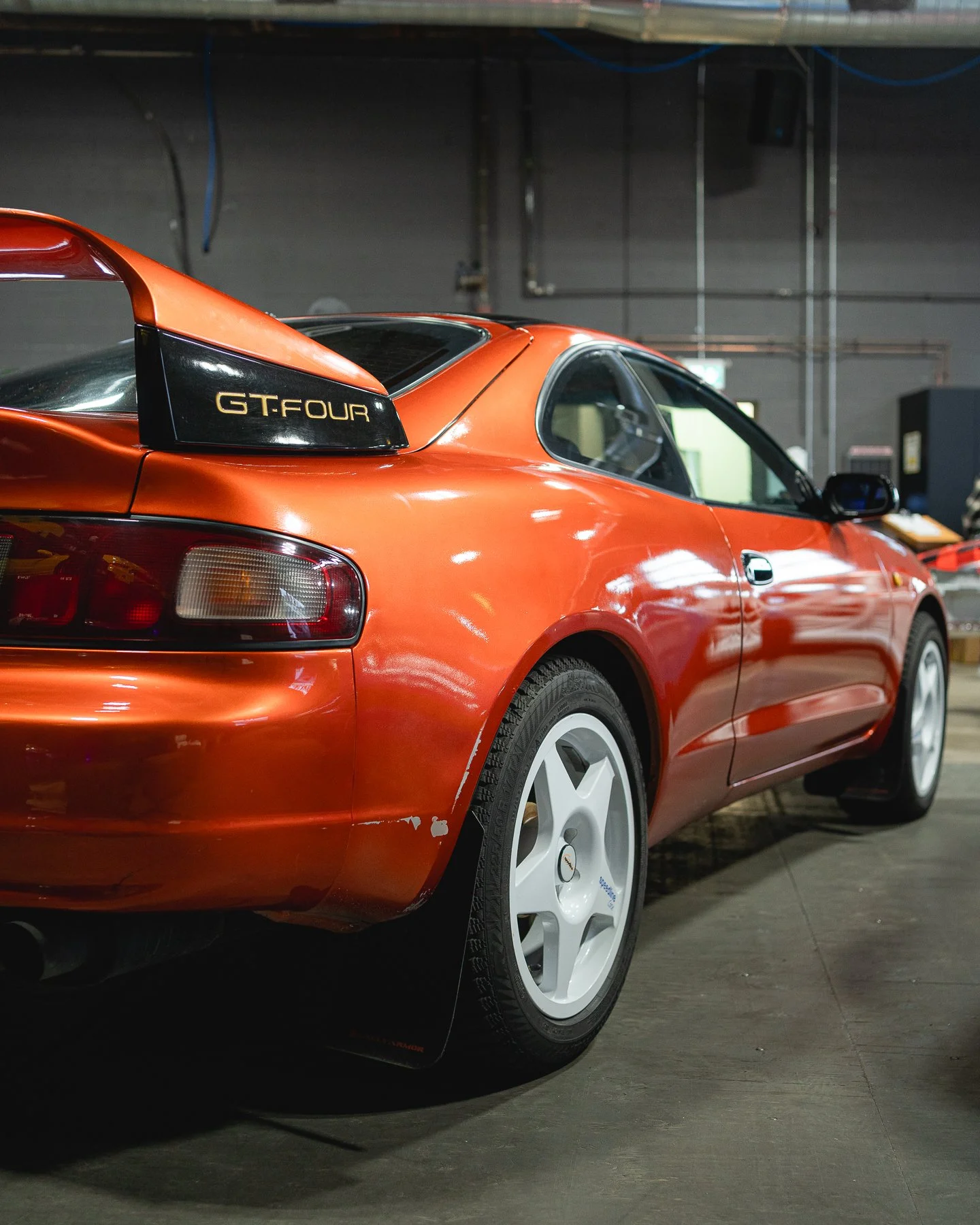 Red sports car with a rear wing labeled 'GT-Four' parked indoors.