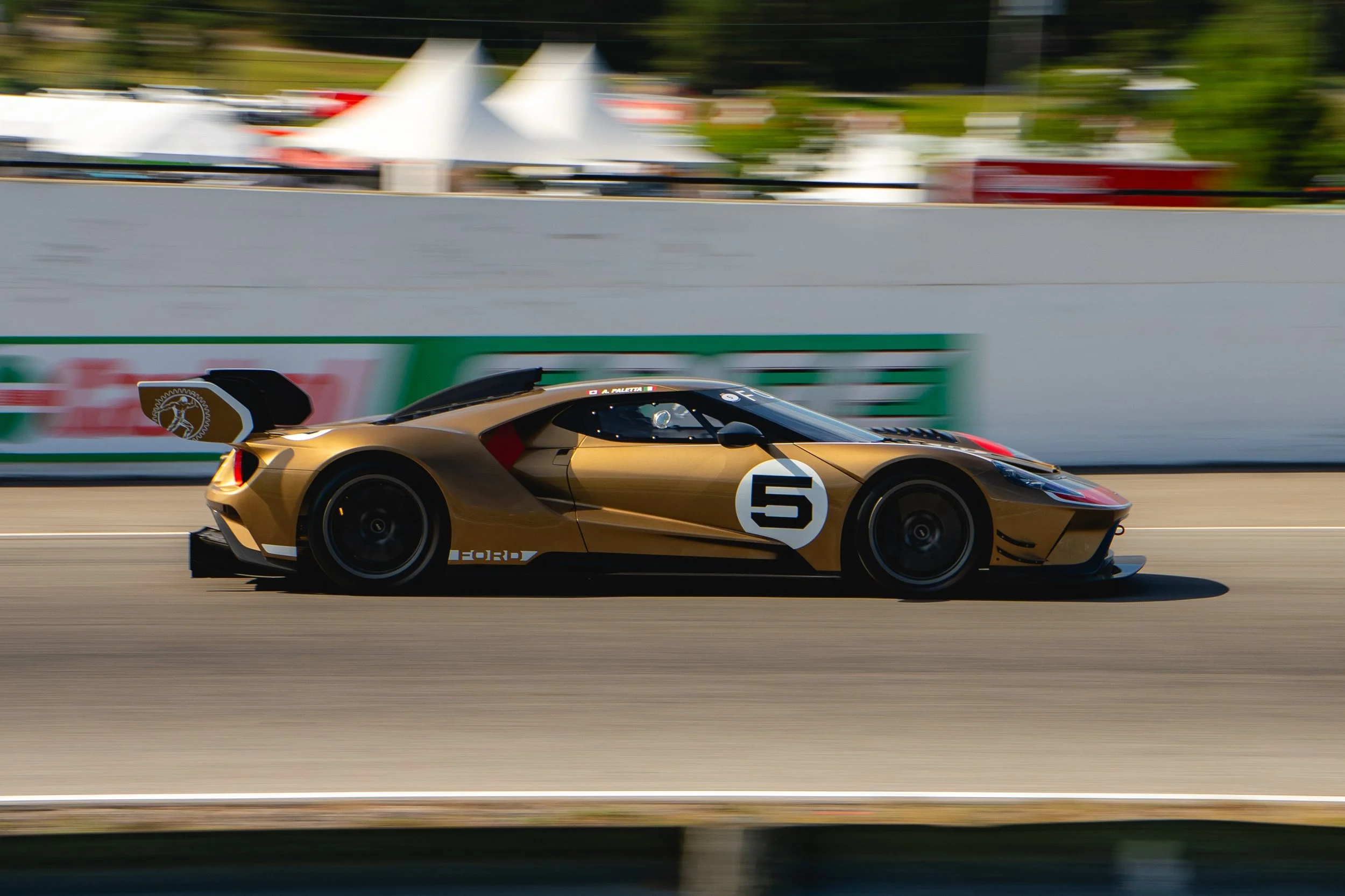 A gold race car with the number 5 on the door driving on a race track.