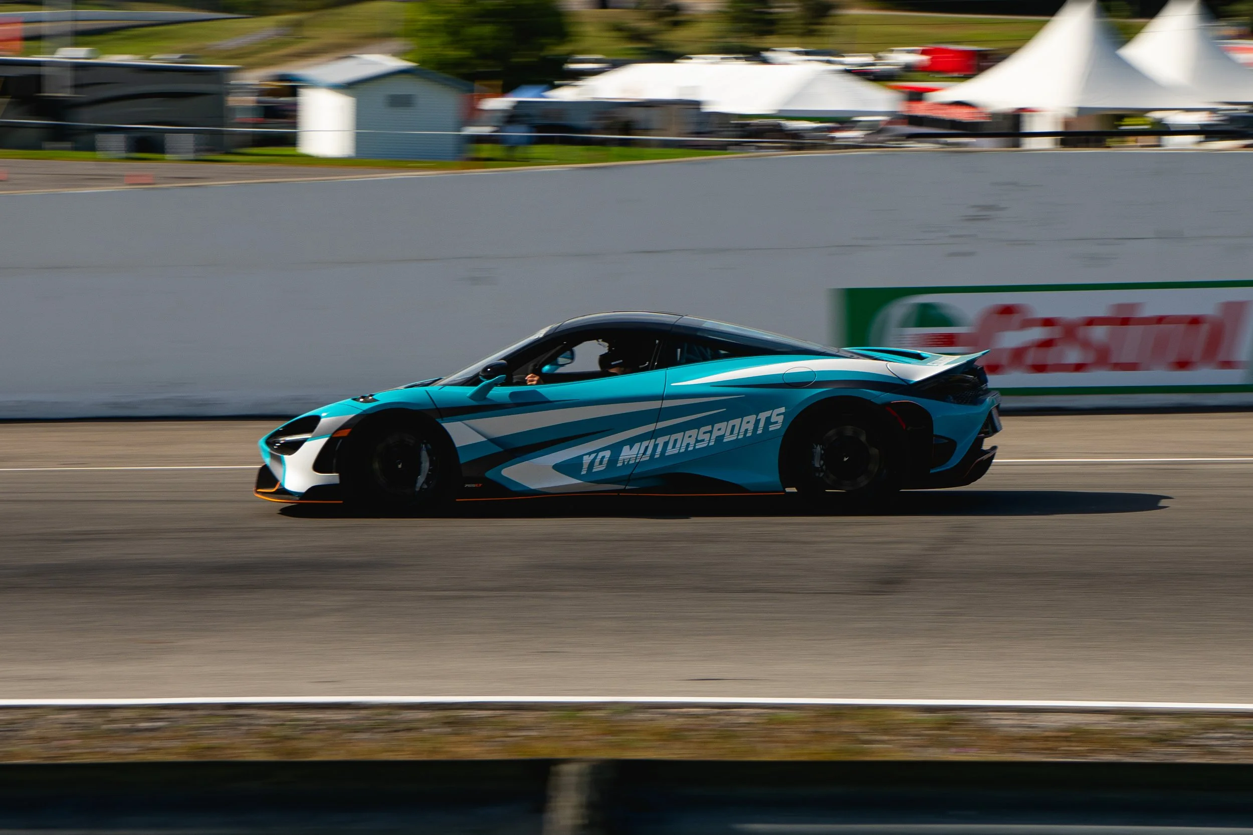 A blue and black race car on a track with the words 'TO MOTORSPORTS' printed on the side, moving at high speed with a blurred background.
