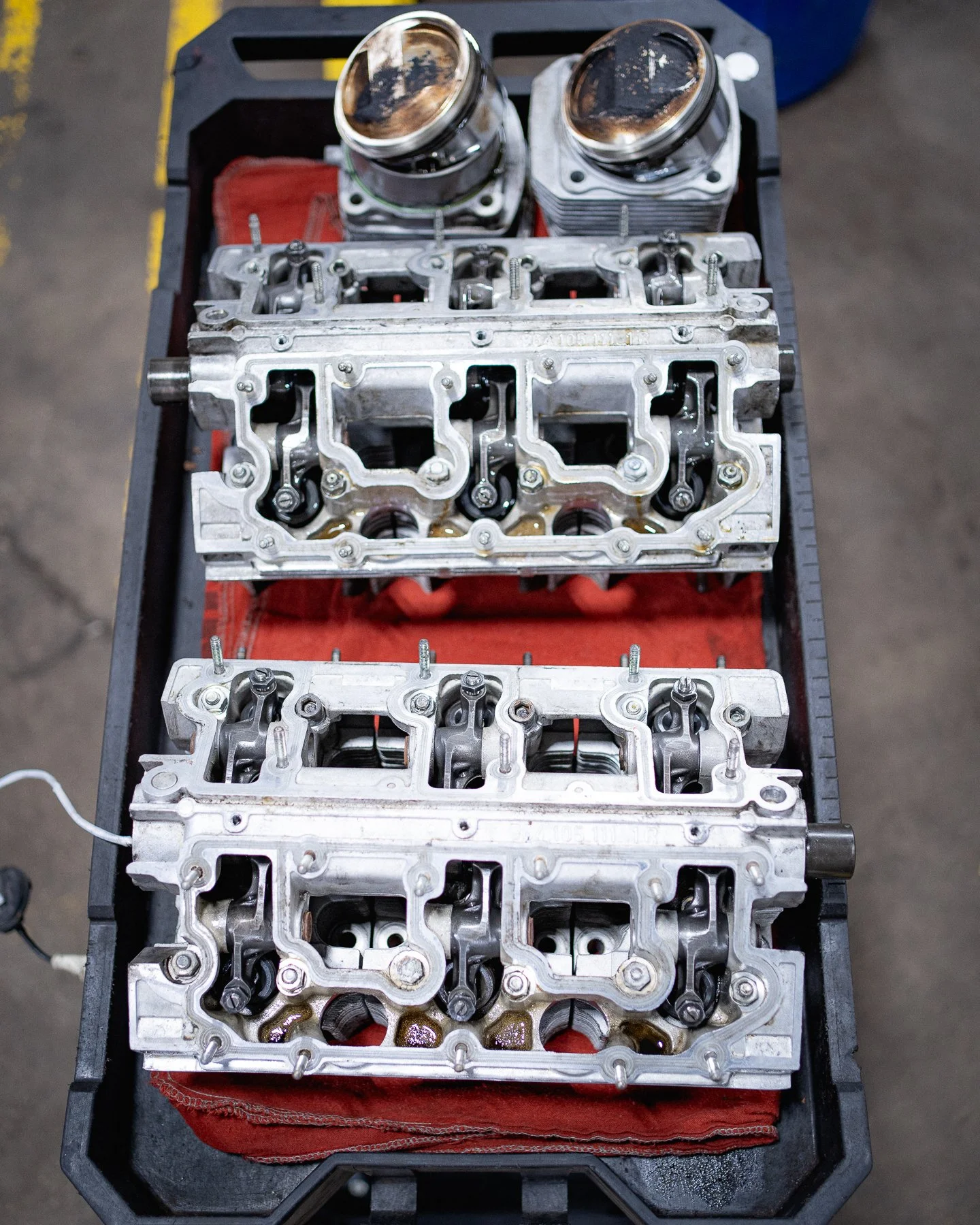 Two metal engine cylinder heads and two pistons placed on a workbench with a red cloth underneath.