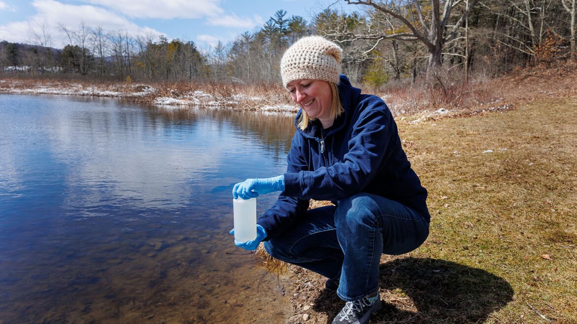 A photo of Dr. Z gathering a water sample from a river near Hartwick..
