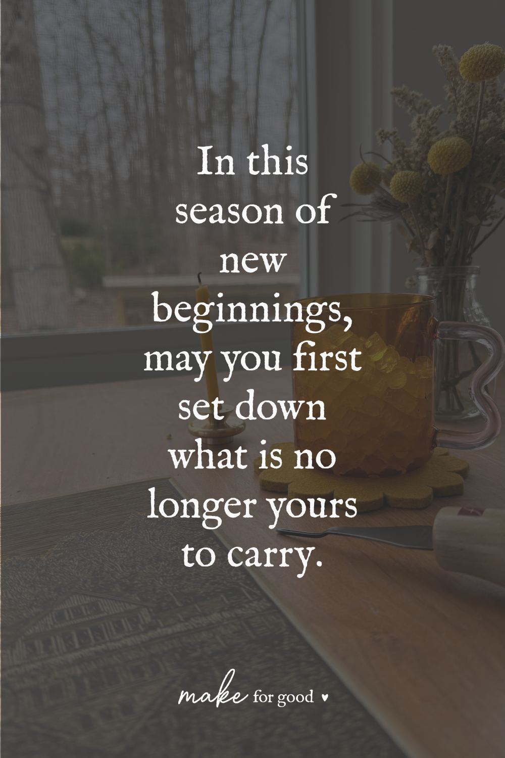 A quiet tabletop scene by a window with an amber glass mug, candle, dried flowers, and tools, featuring text that reads “In this season of new beginnings, may you first set down what is no longer yours to carry.”