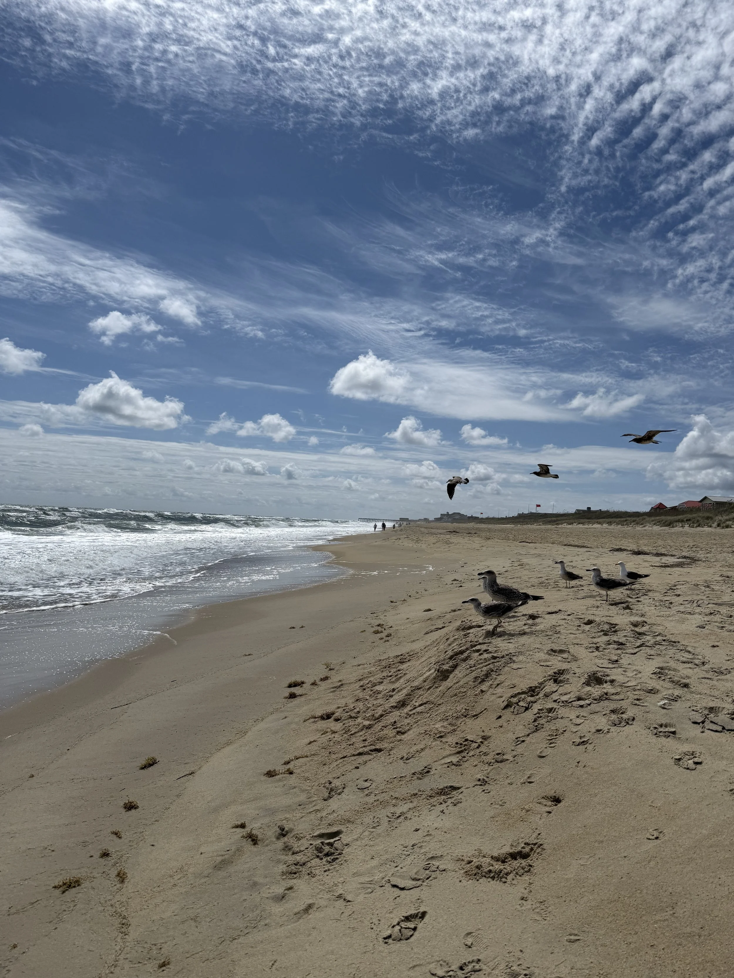 Ocean waves crashing near a wooden pier under a wide sky during a quiet morning in the Outer Banks, North Carolina