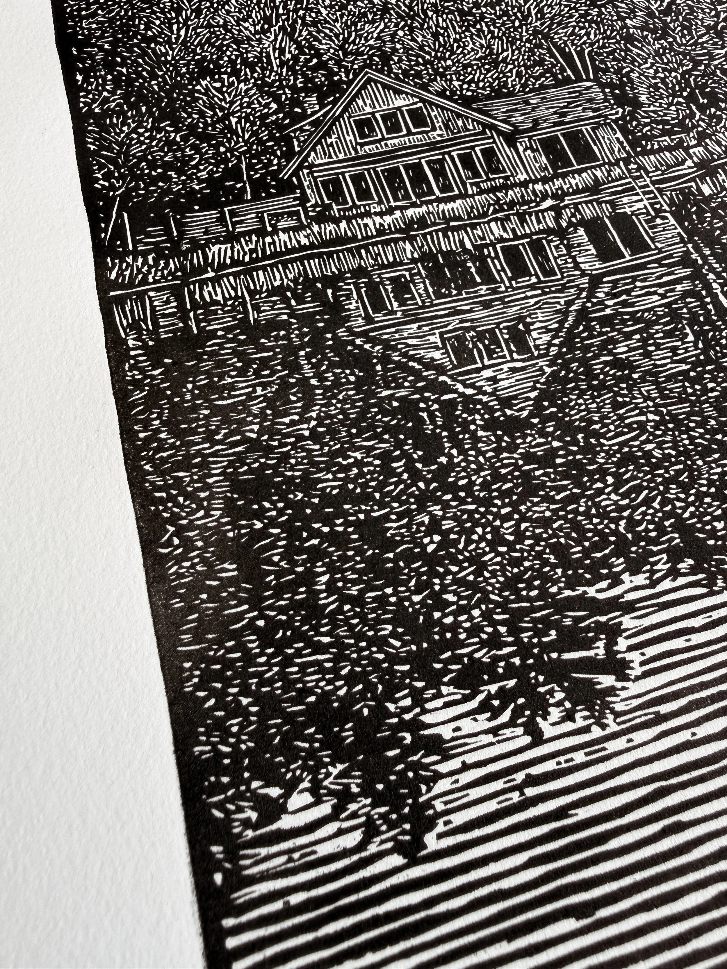 Close-up of linocut print showing cabin reflection and detailed carved linework in still water