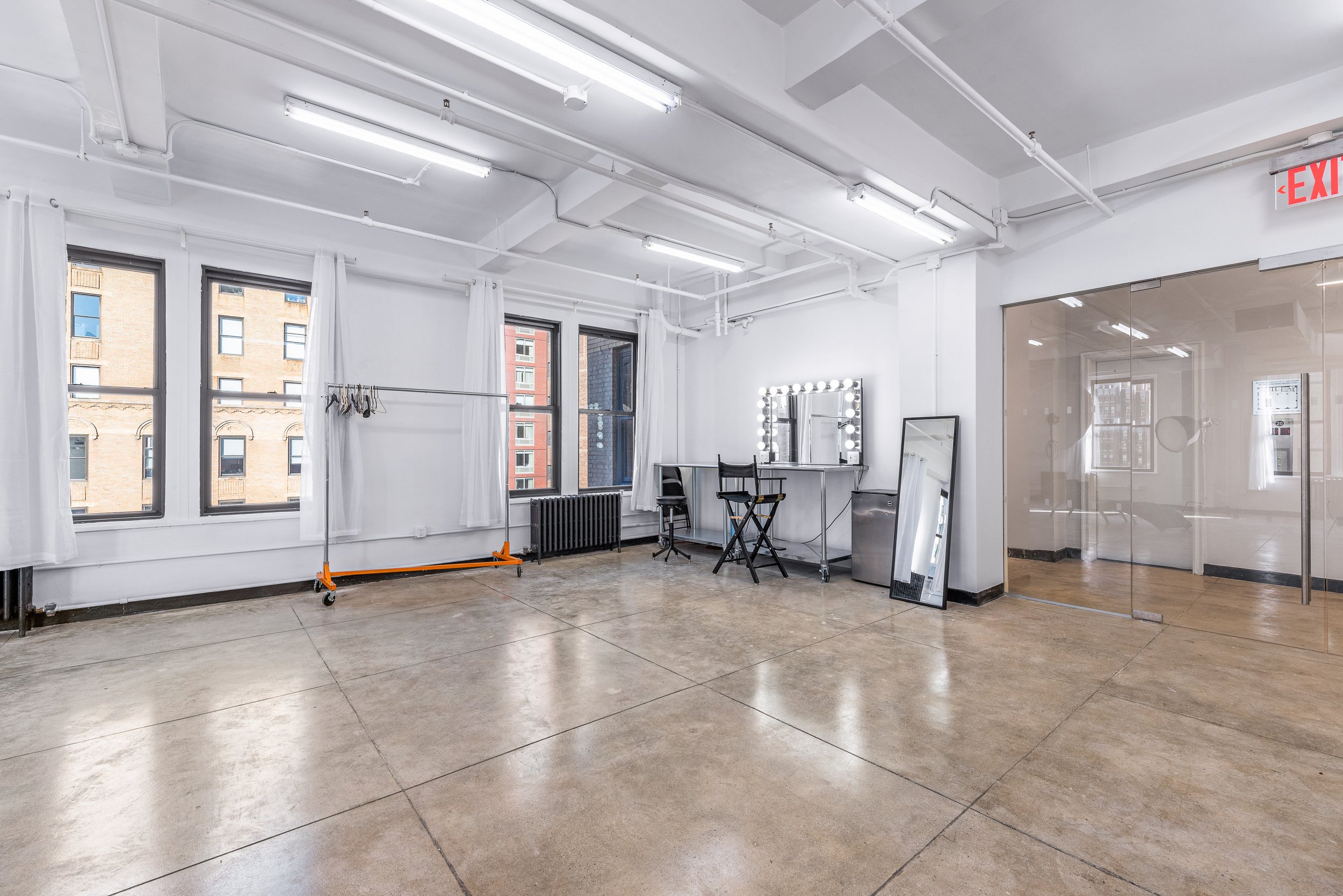 Spacious bright room with large windows, makeup vanity, director's chair, clothing rack, and full-length mirror.
