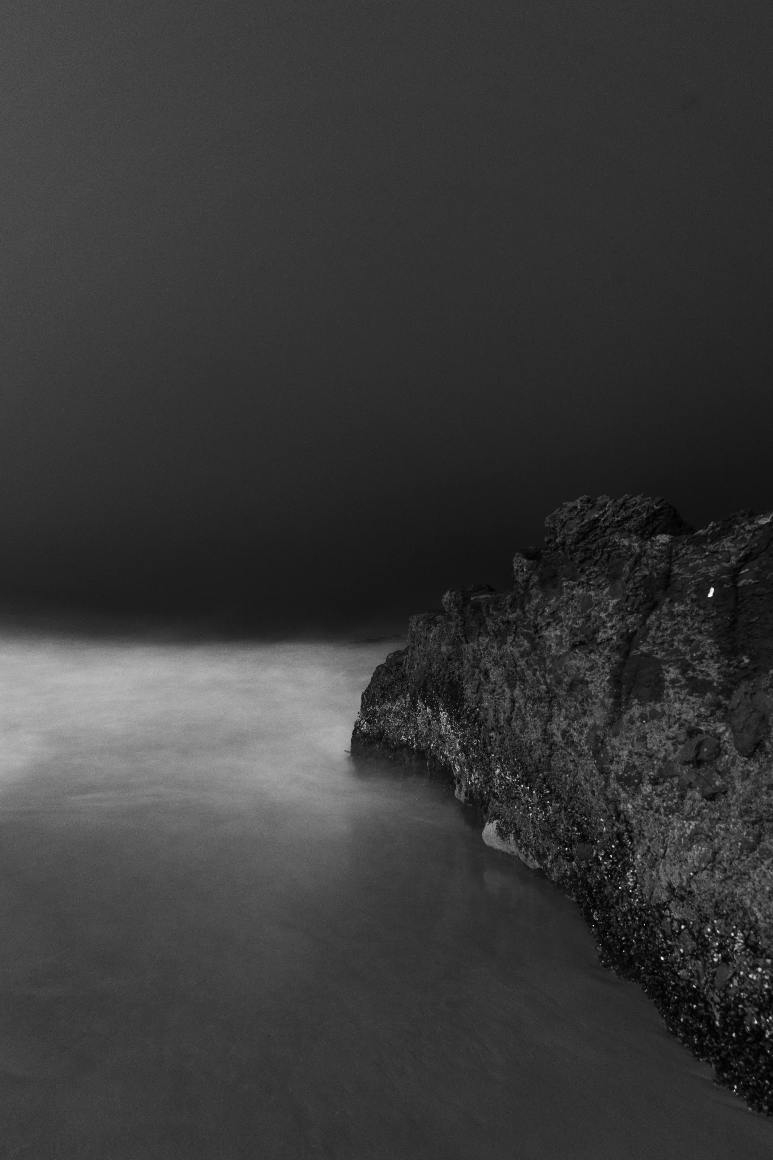 Black and white photograph of coastal rock formation and calm water at night.
