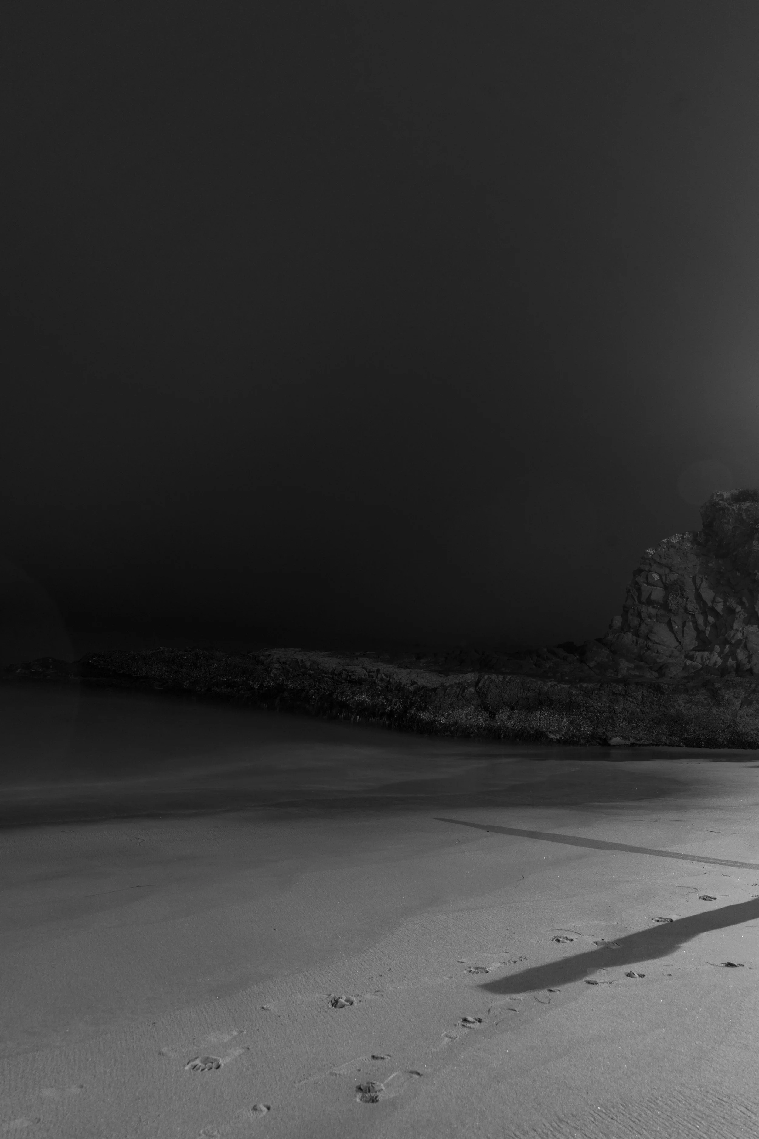 Black and white beach scene with rocks and footprints