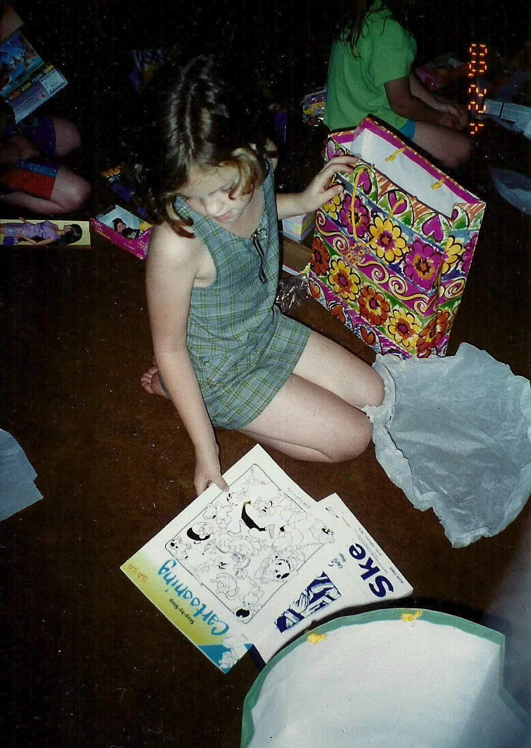 A young girl sitting on the floor surrounded by Christmas gifts, holding a cartoon drawing guide.