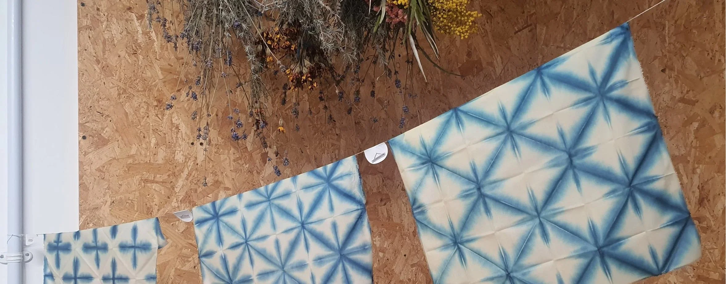 Three indigo blue patterned cloths on a washing line in front of a brown wood background.