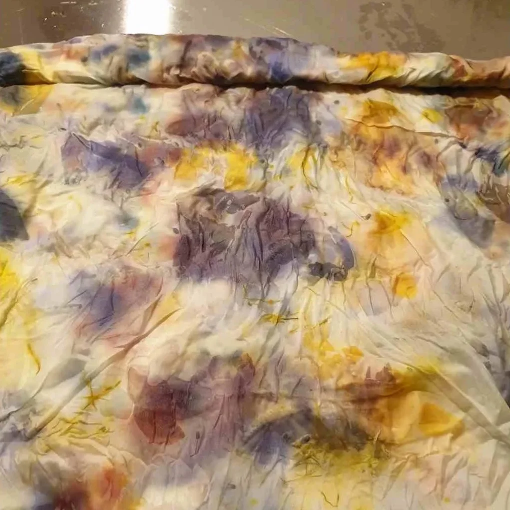 patterned silk scarf being unrolled on a stainless steel surface.